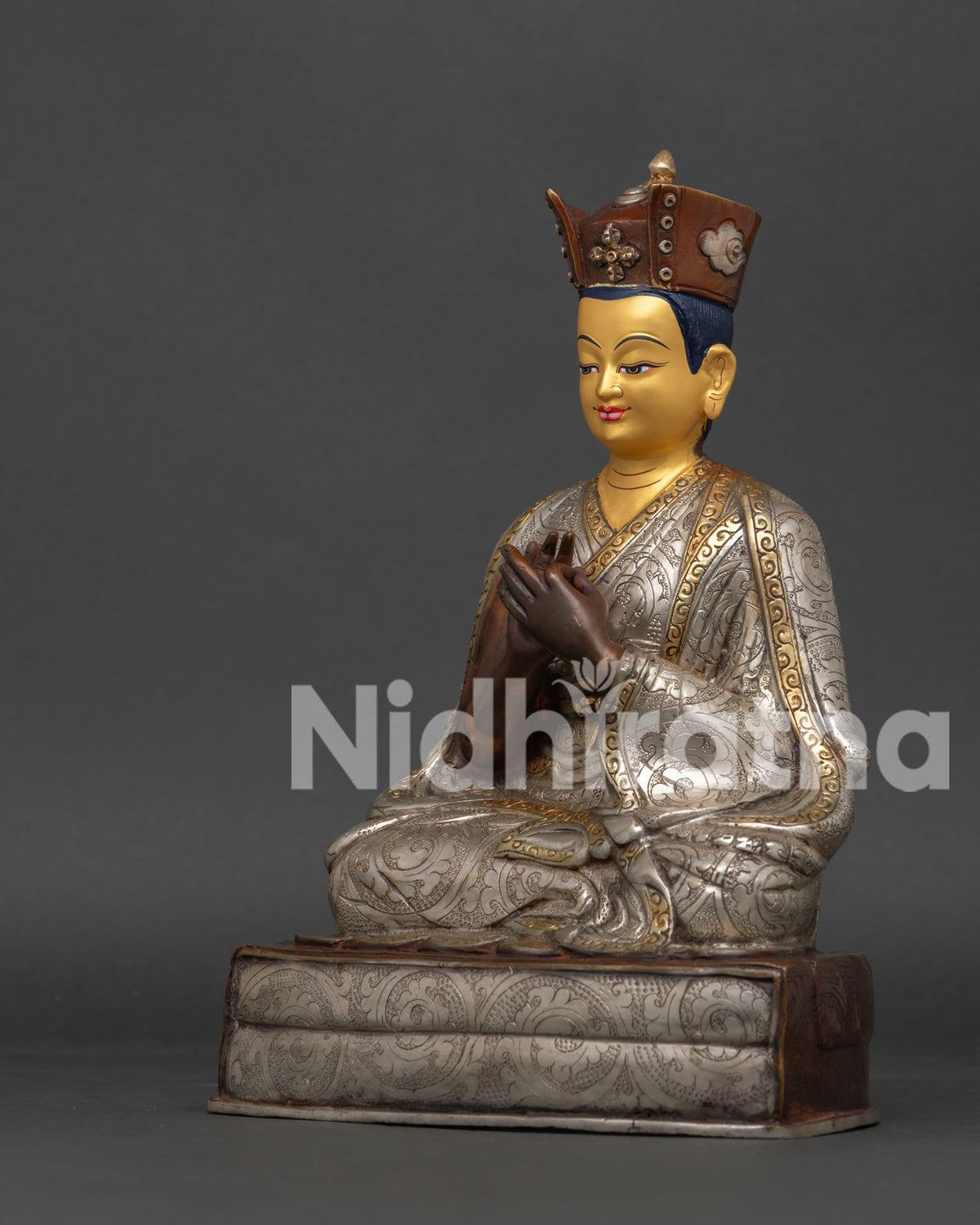Side view of Karmapa Buddhist statue with silver plated finish and ornate pedestal.