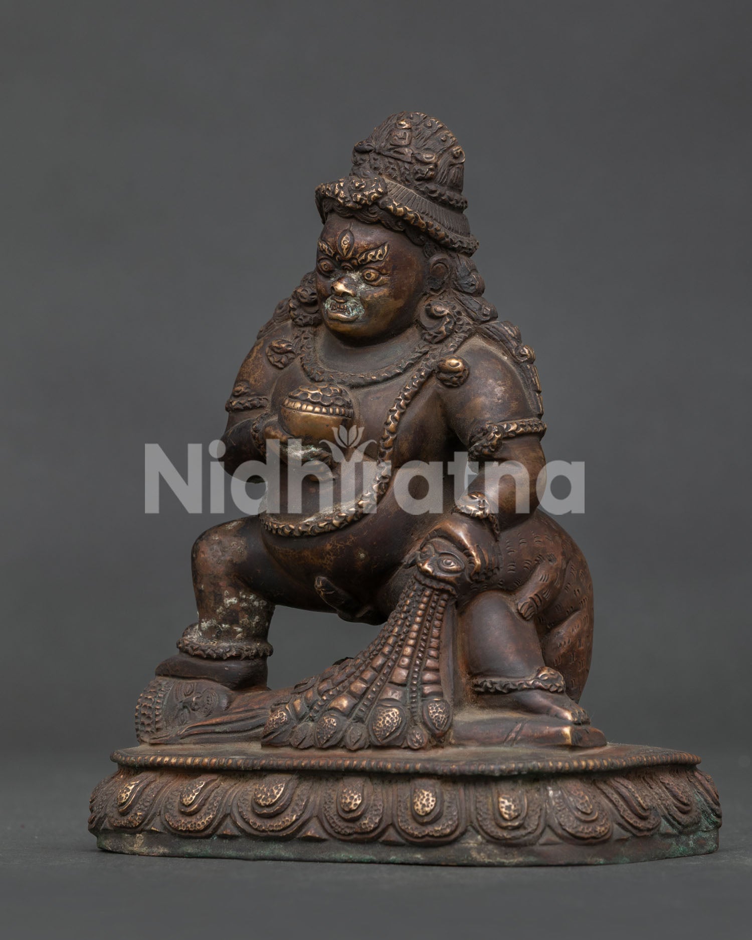 Side view of Black Dzambhala Statue standing over subdued figure on lotus pedestal.