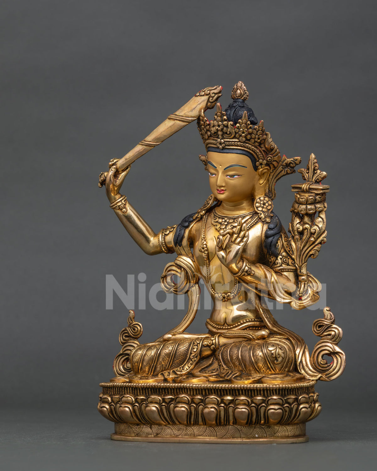 Side view of manjushri statue with hand carved lotus pedestal and floral silk garment.