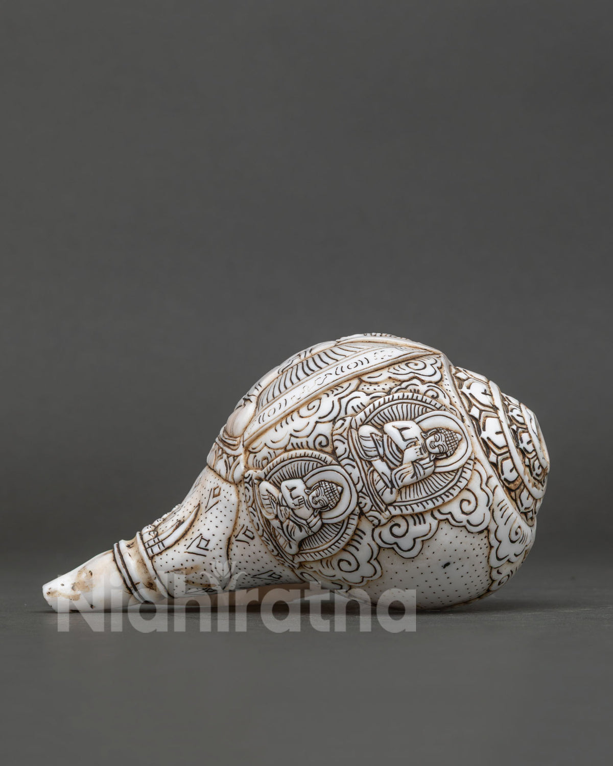 Side view showing two carved meditating Buddha figures on white conch shell.