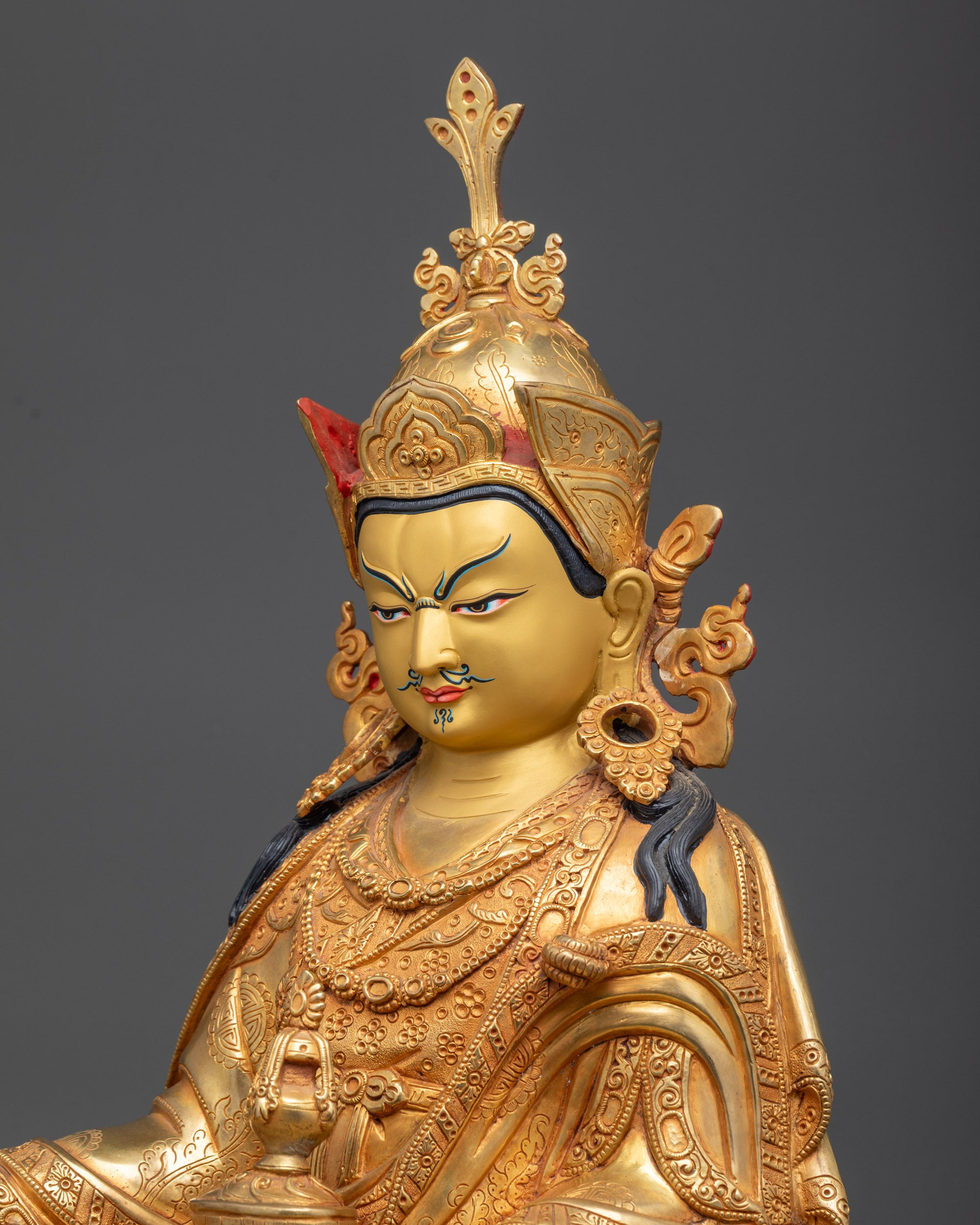 side close up face Guru Rinpoche statue showing gold gilded facial details and crown