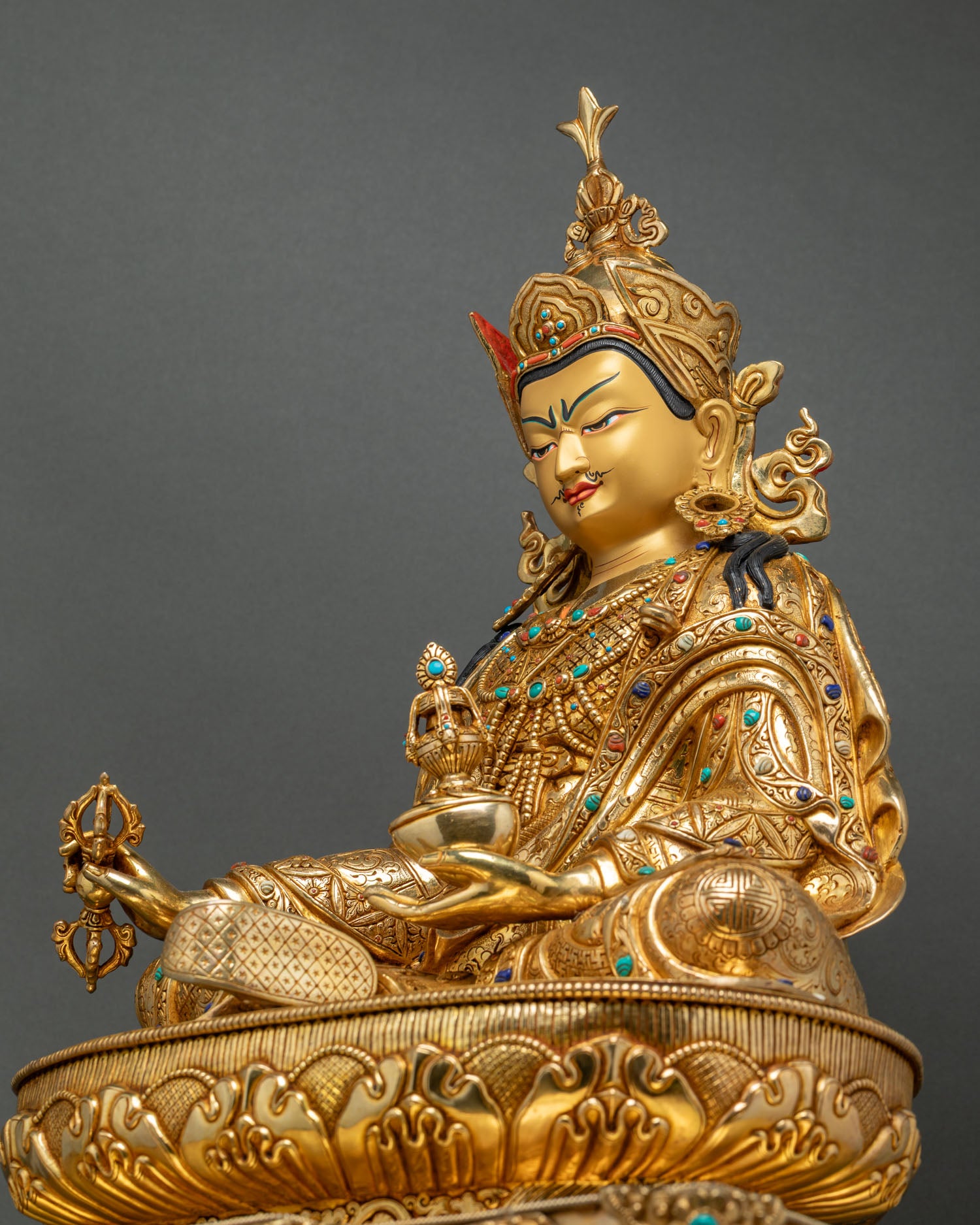 Three-quarter view of Guru Rinpoche statue holding khatvanga staff and vajra