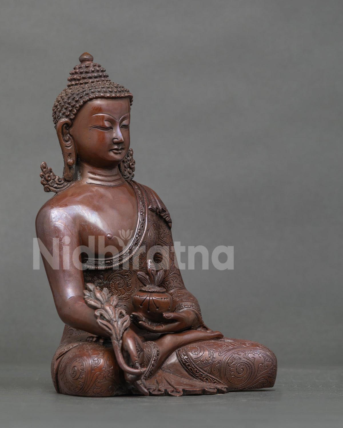 Three-quarter view of oxidized copper Bhaisajyaguru statue with myrobalan plant in hand