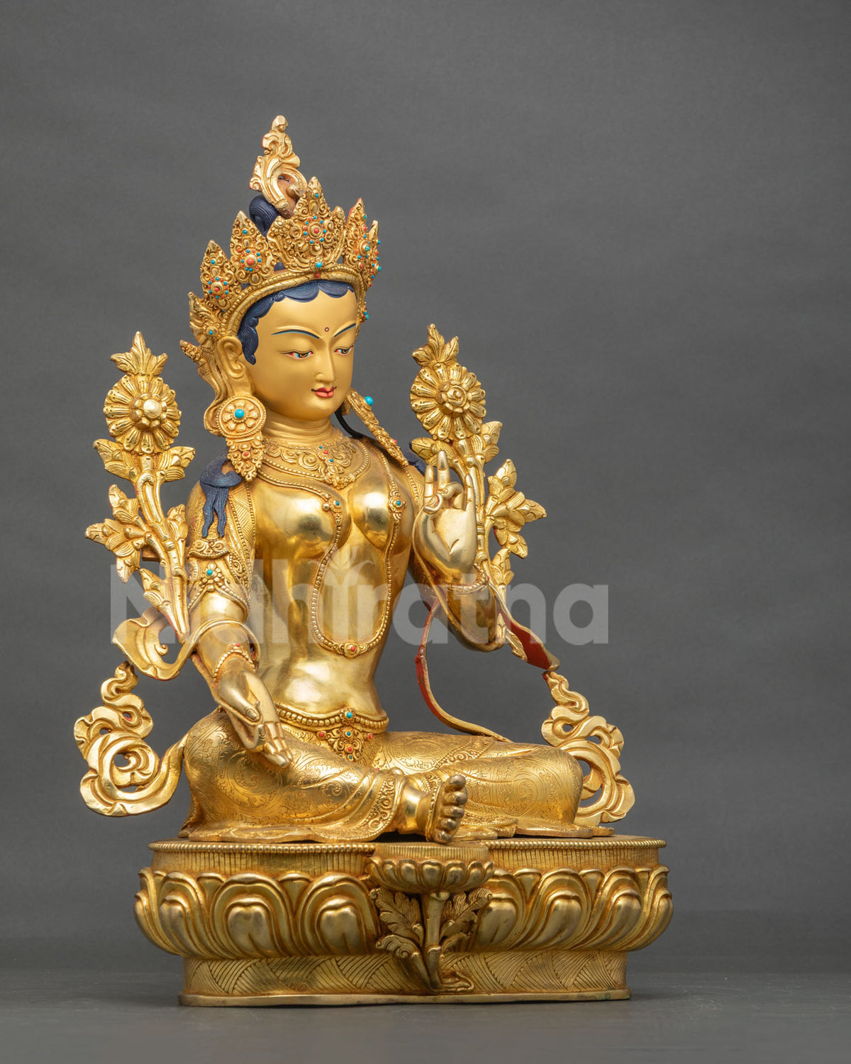 Three-quarter view of the gold fire gilded Green Tara statue with blooming lotus flowers on a lotus base