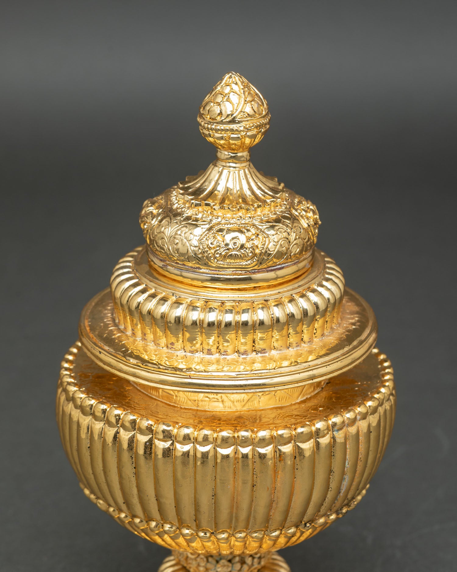 Tibetan ritual rice pot resting on sacred altar base featuring floral designs and traditional Newari metal craft detailing