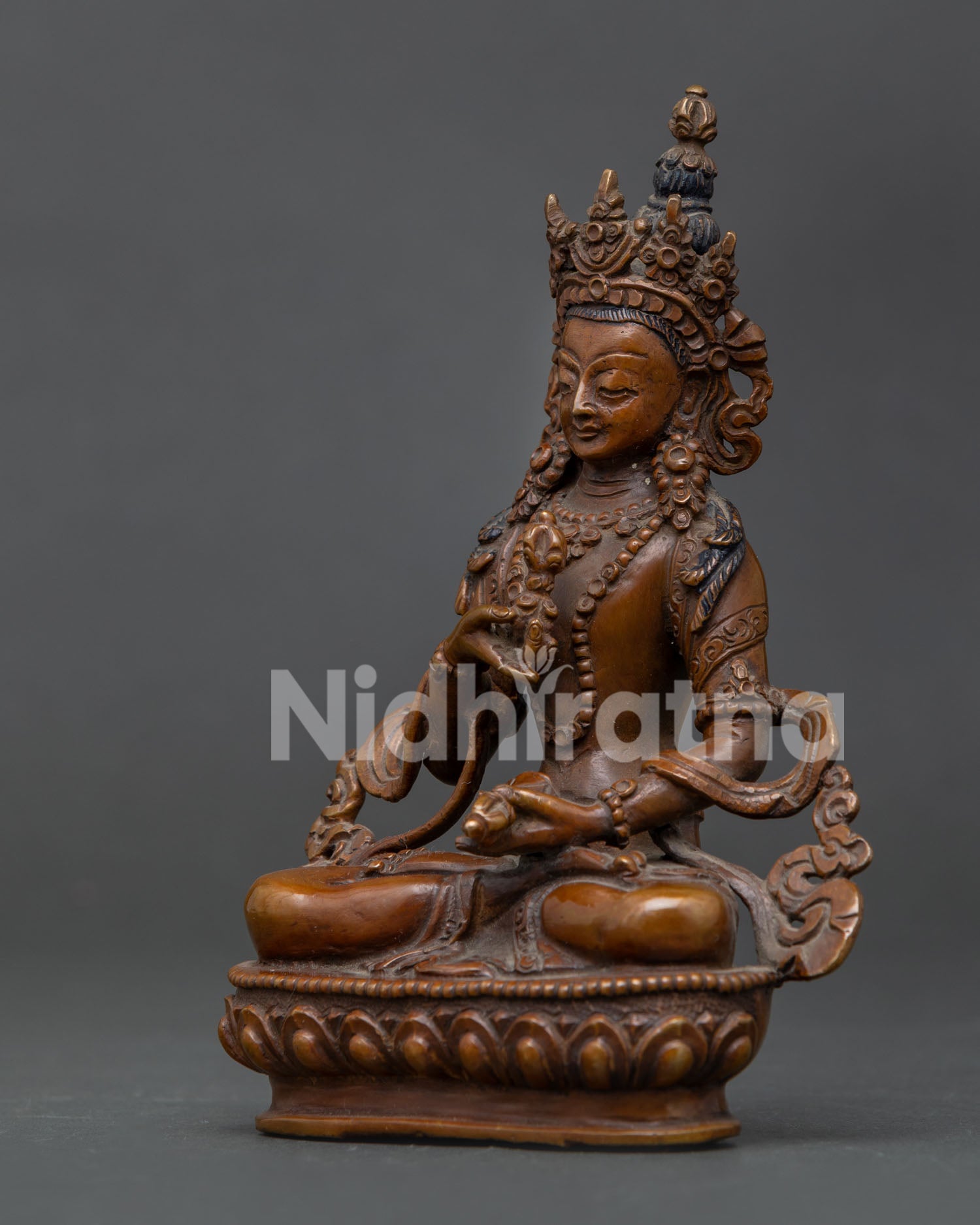 Vajrasattva statue holding vajra and bell in oxidized copper finish.