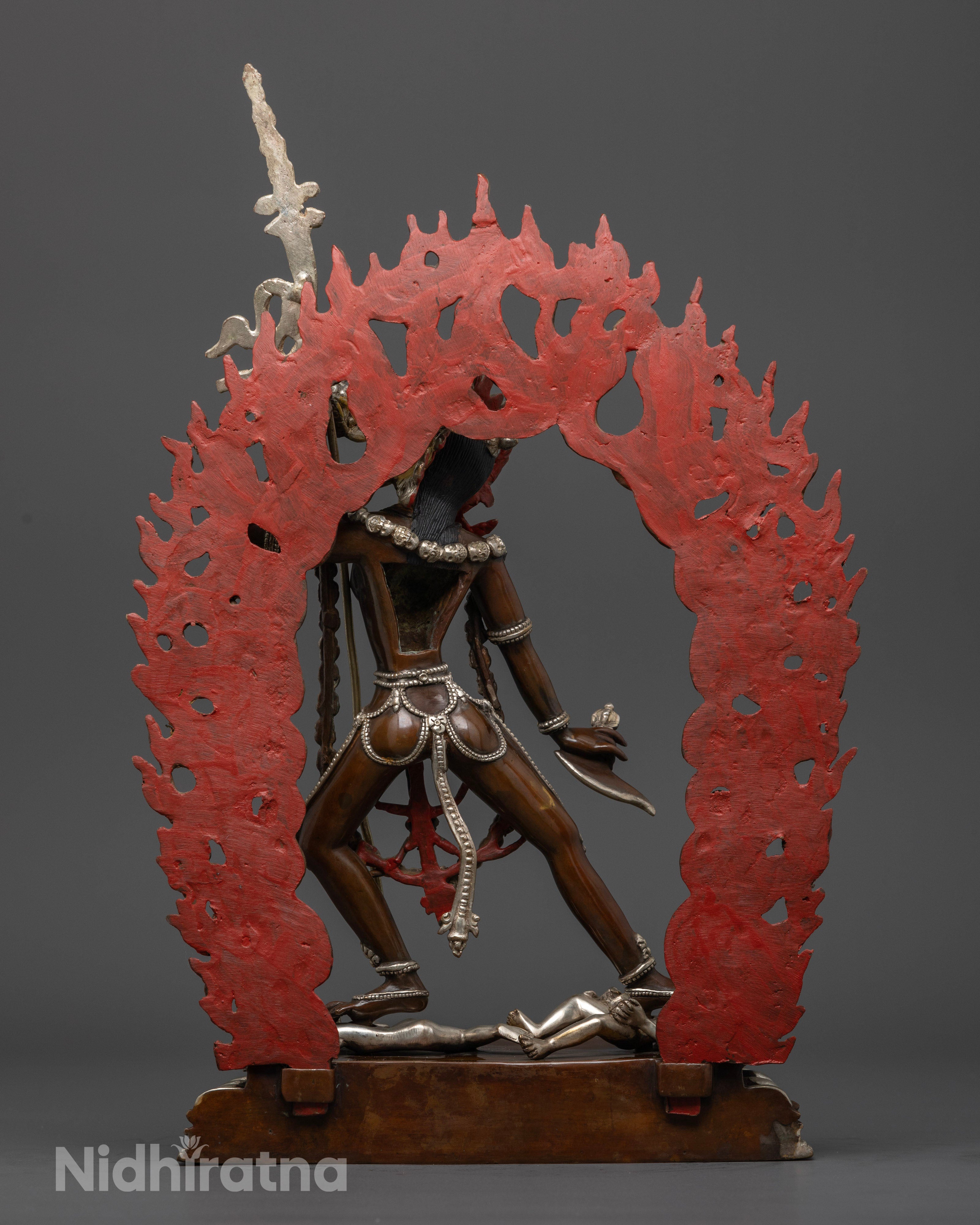 Vajrayogini statue, silver-plated with vibrant acrylic colors, standing gracefully on two men, symbolizing mastery over obstacles and the transformation of negative energies into spiritual power."