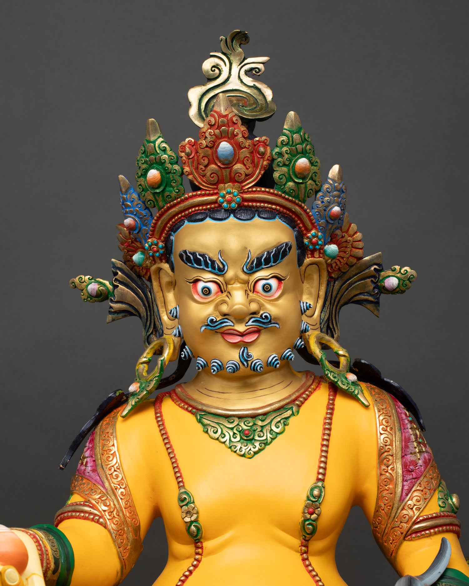 Yellow Dzambhala statue close-up, gold-painted face, jeweled ornaments, prosperity-bringing attributes detailed
