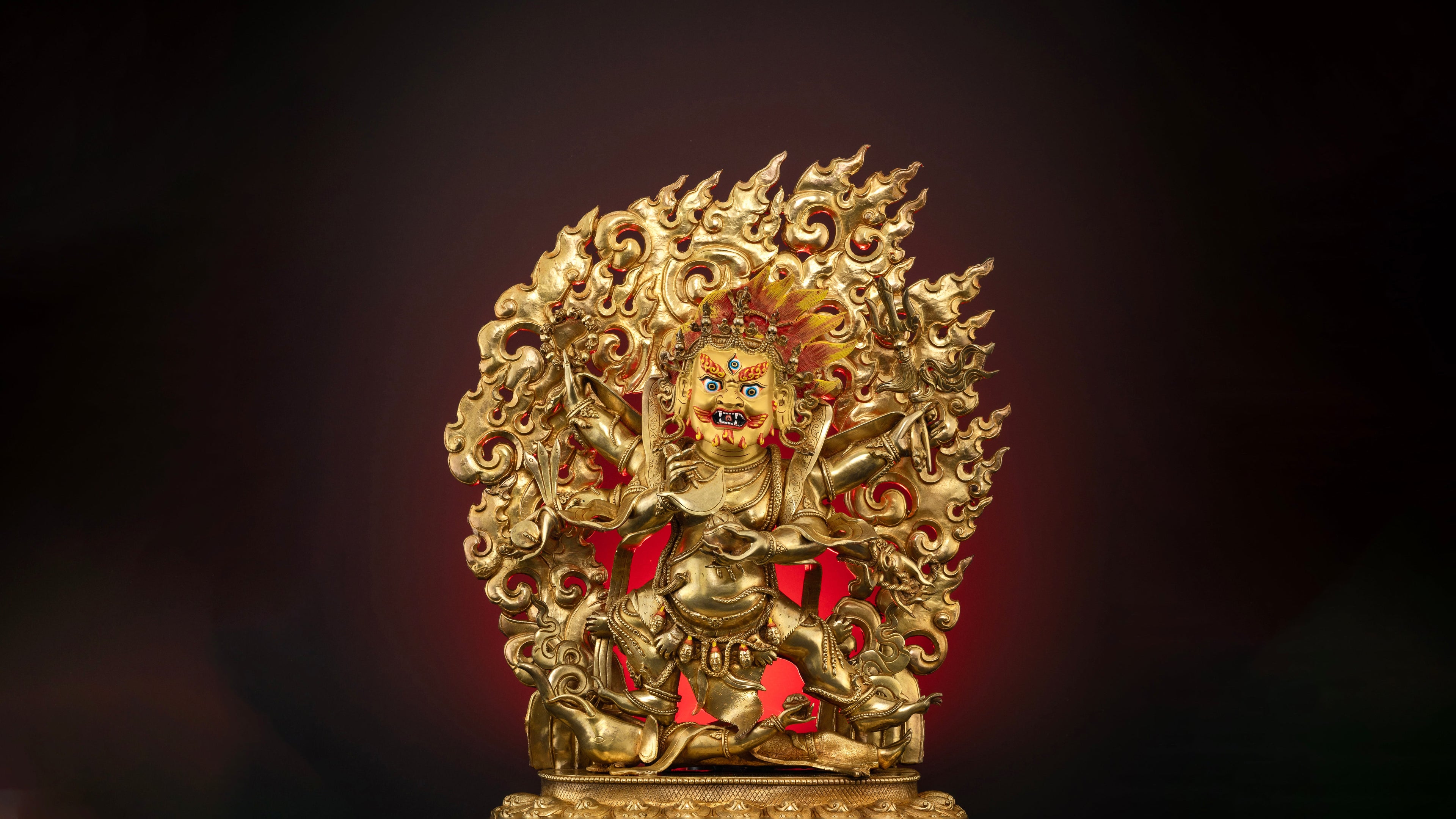 Gold plated six armed mahakala statue with pure gold coated face on a dark background