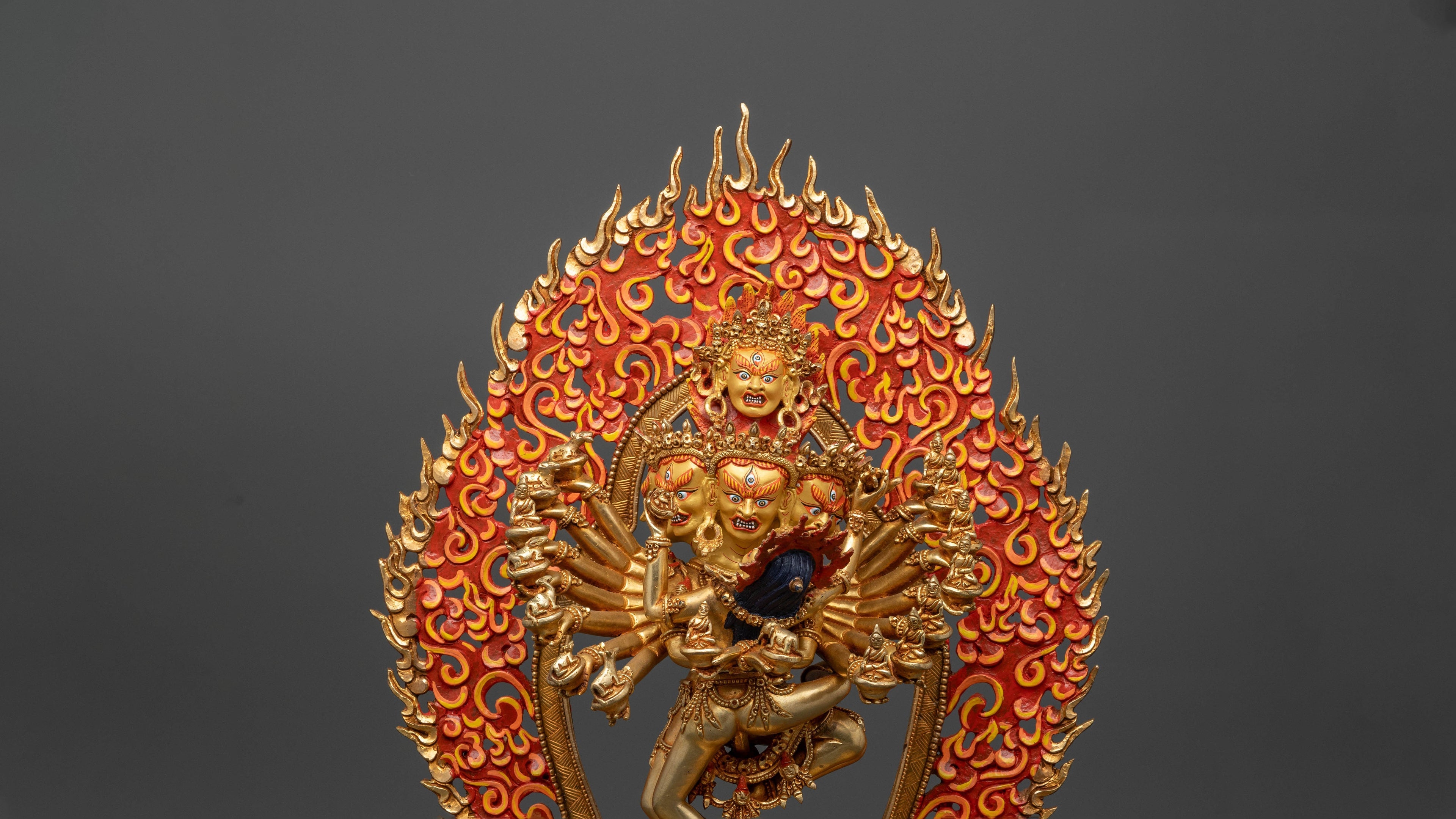 Many armed Hevajra statue with his consort. The statue is golden with a fiery background and has many faces all in wrathful positions