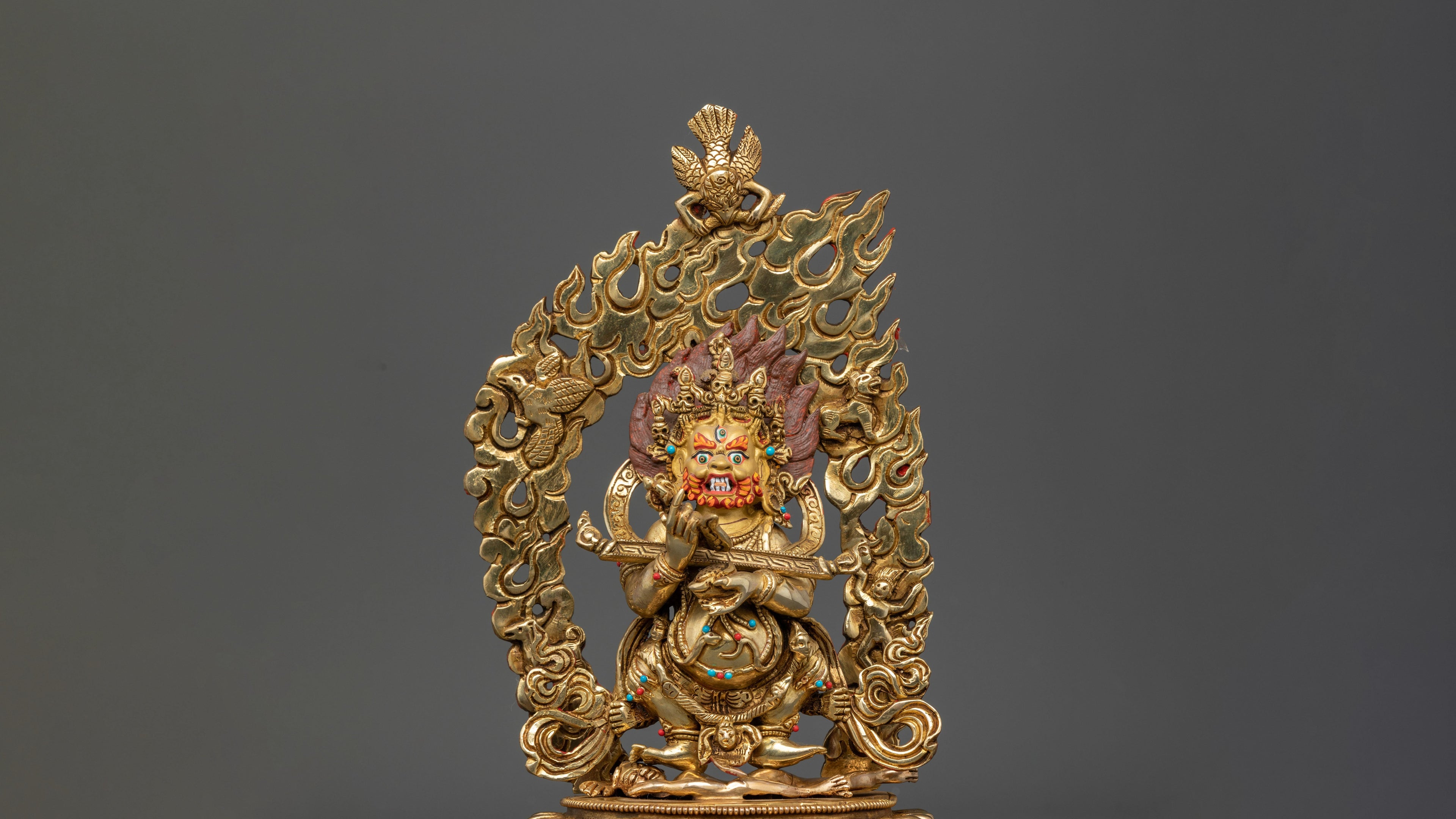 golden statue of Sakya Mahakala in his wrathful form with fire in the background