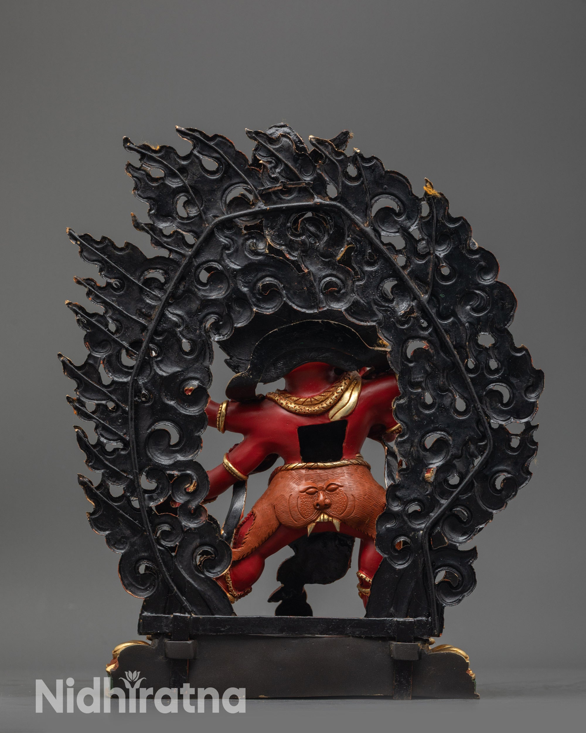 Back view Red Dzambhala statue with flaming halo and miniature garuda on lotus seat