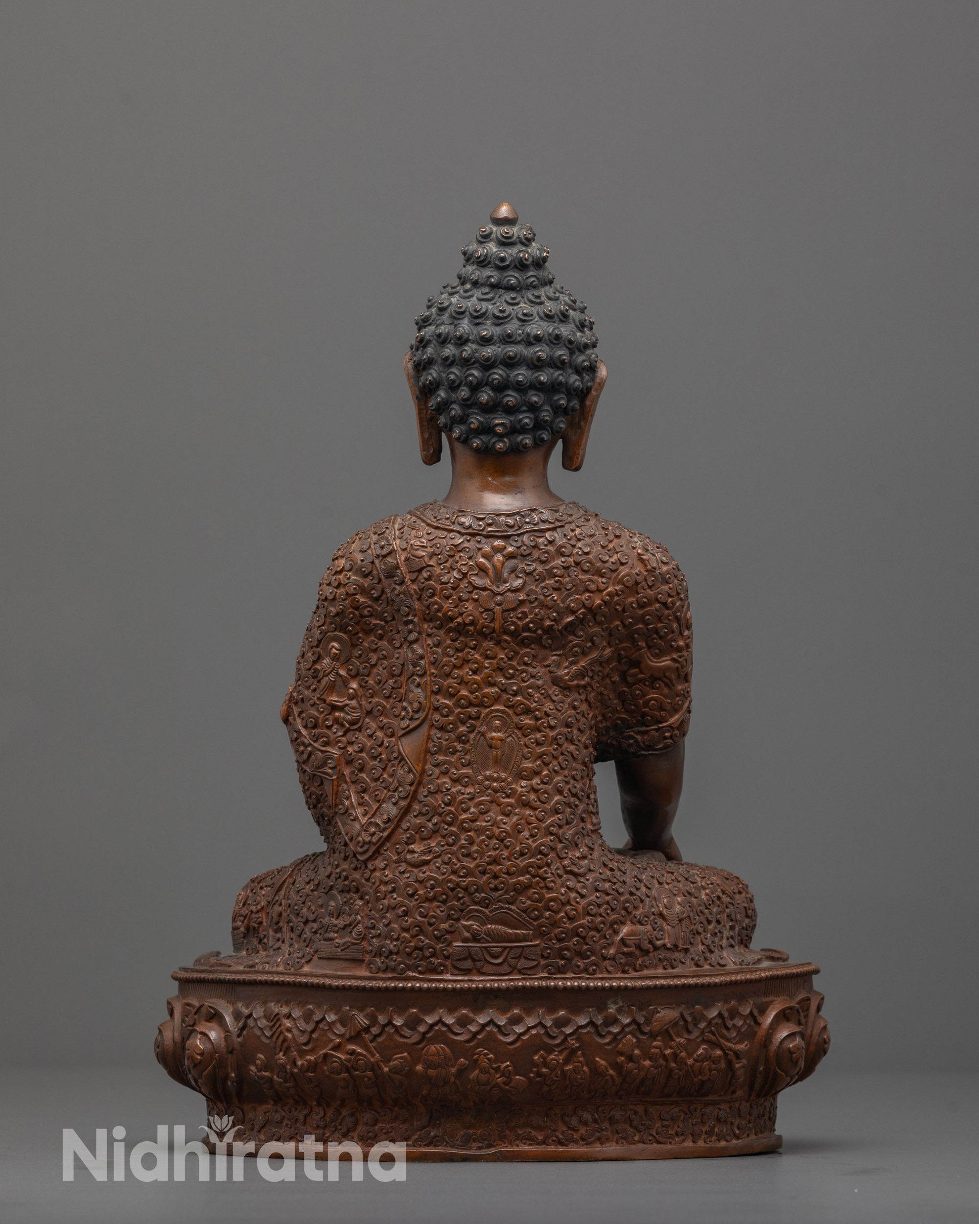 Back view of Buddha statue displaying intricate patterns and miniature deities on robe and seat.
