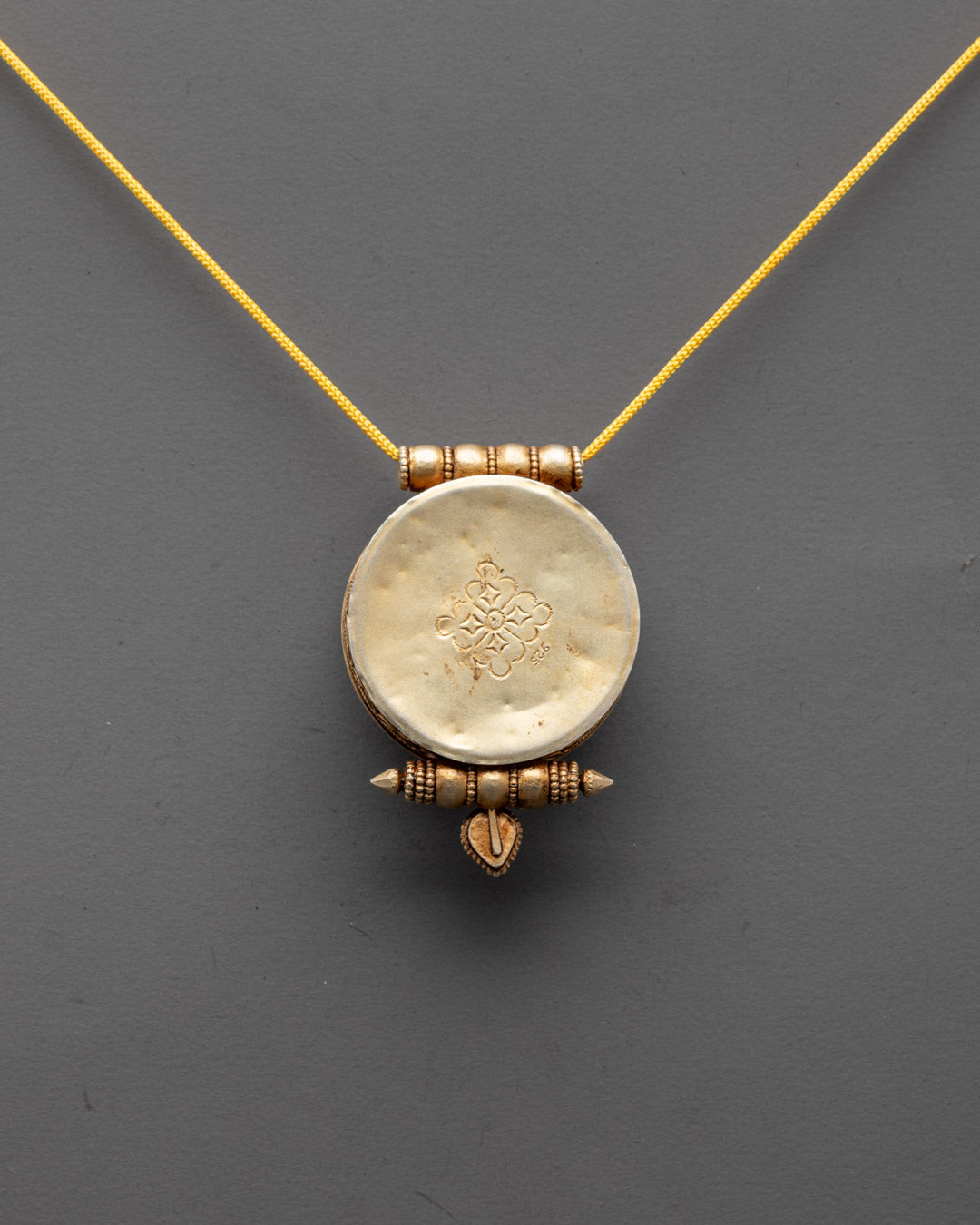 Back view of sacred Tibetan pendant featuring traditional symbols and radiant gold plating


