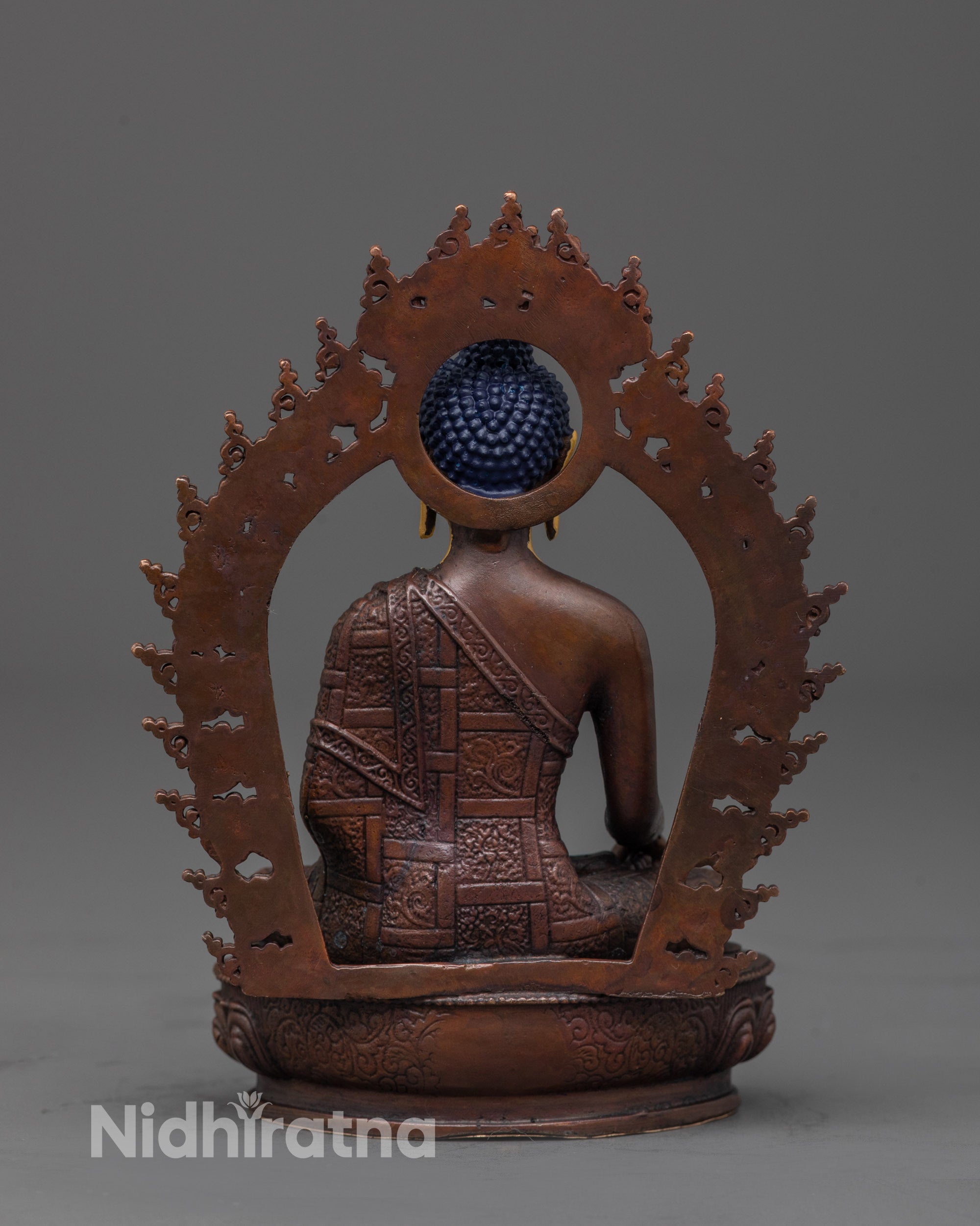 back view of Buddha Shakyamuni statue showing carved robes and oxidized copper brown finish