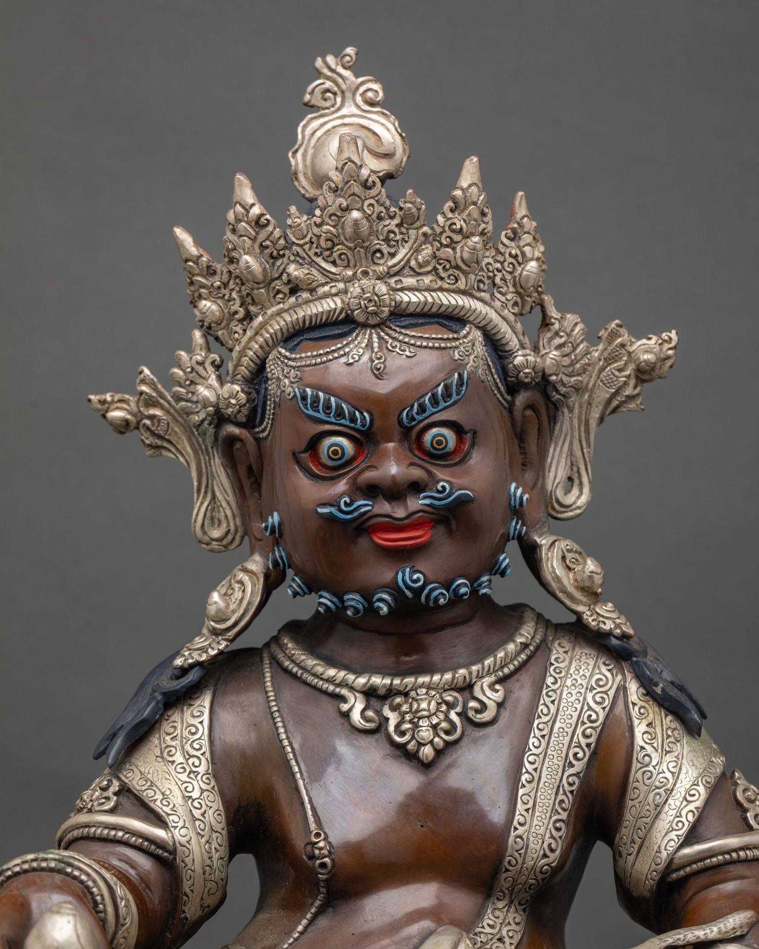 Close up of Dzambhala statue showing wealth deity attributes silver-plated details and lotus seat