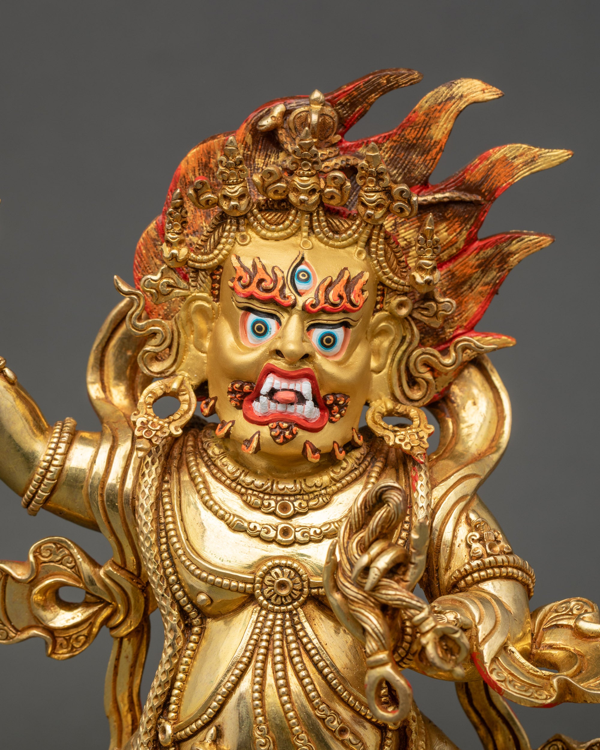 Close-up of Vajrapani statue showing gold-painted face, crown, jewelry, and flowing robe