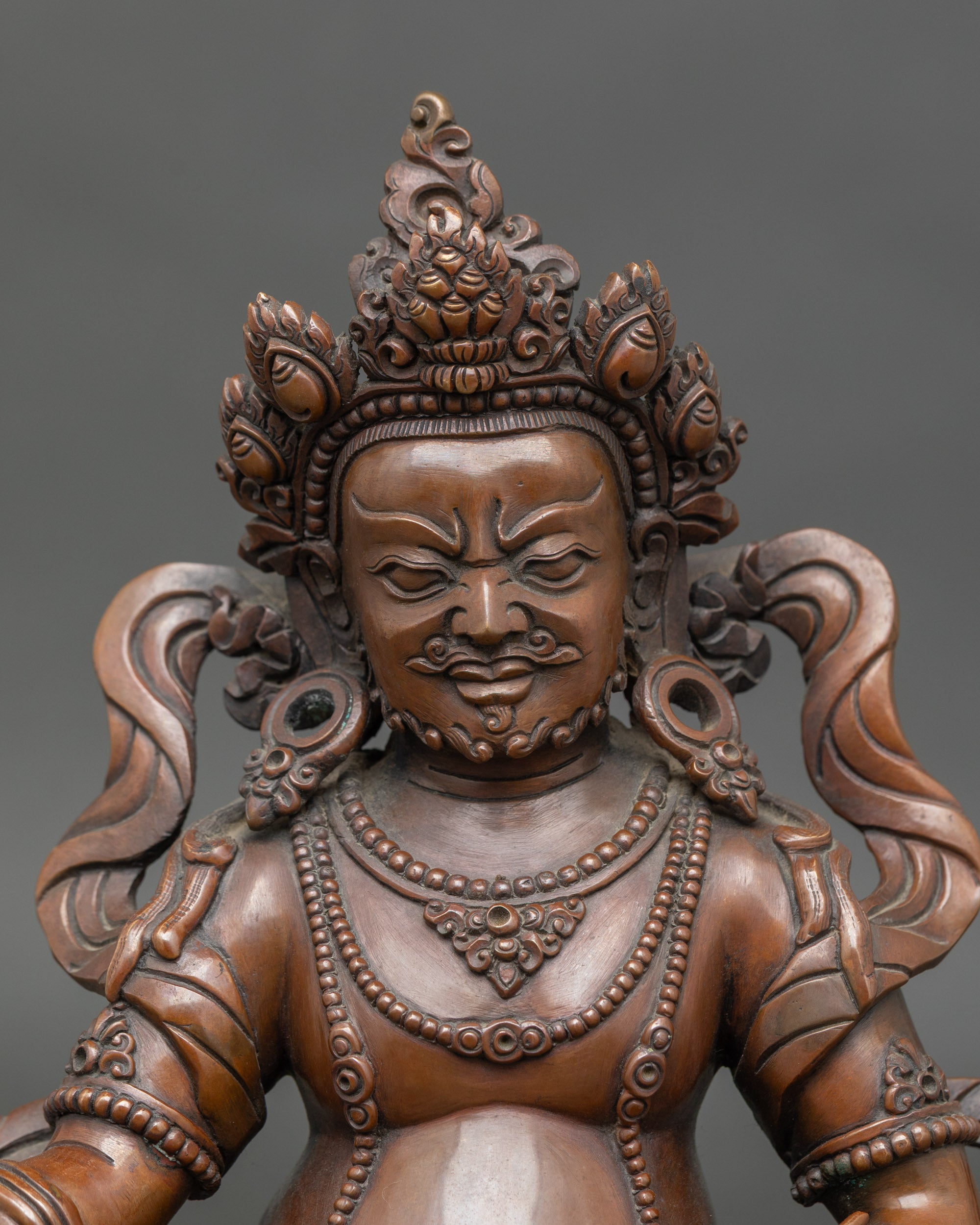 Close-up of Dzambhala Buddha holding jewel-spitting mongoose, oxidized copper details