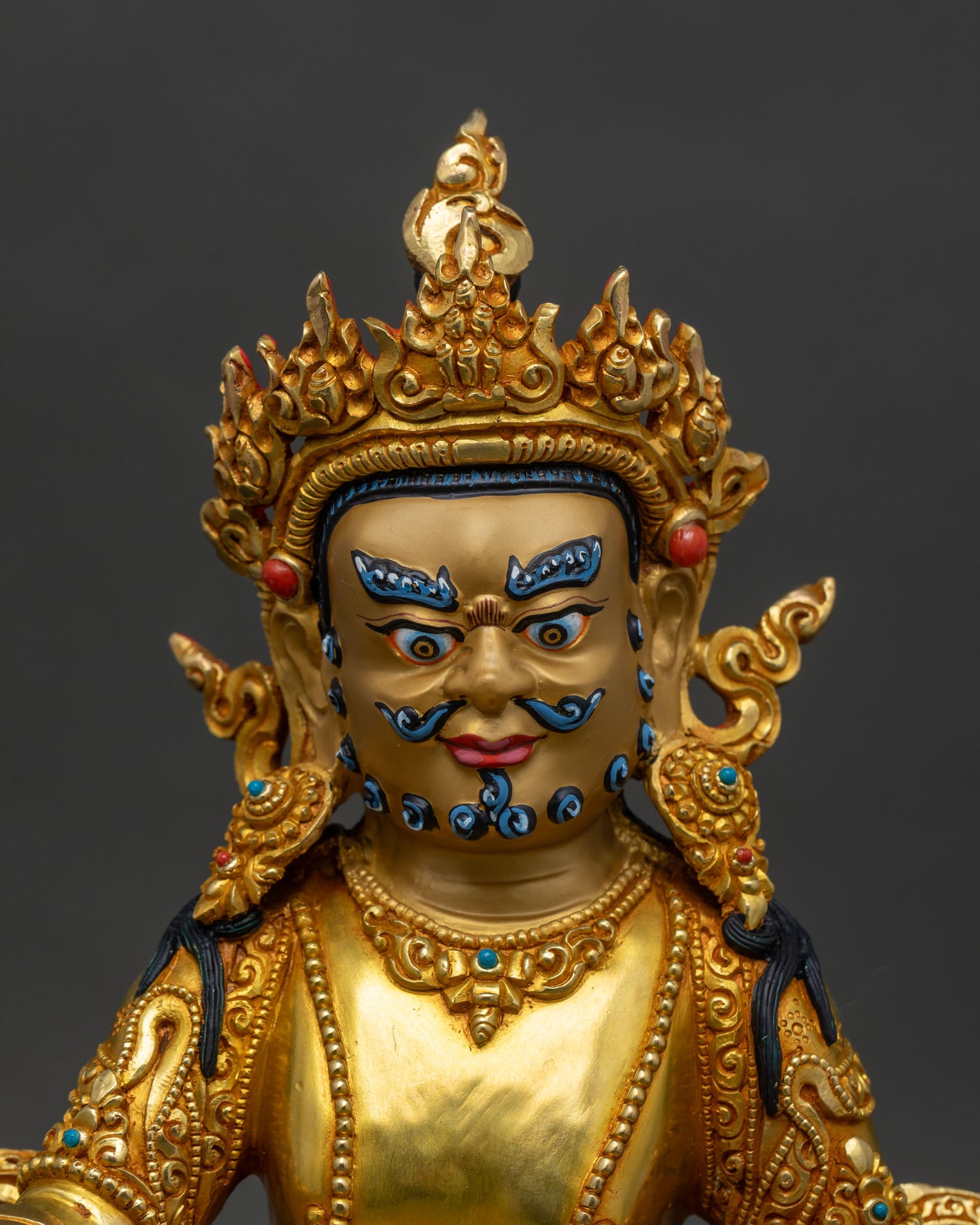 Close up of Dzambhala Statue gold-painted face holding citrons precious jewels sacred Buddhist deity