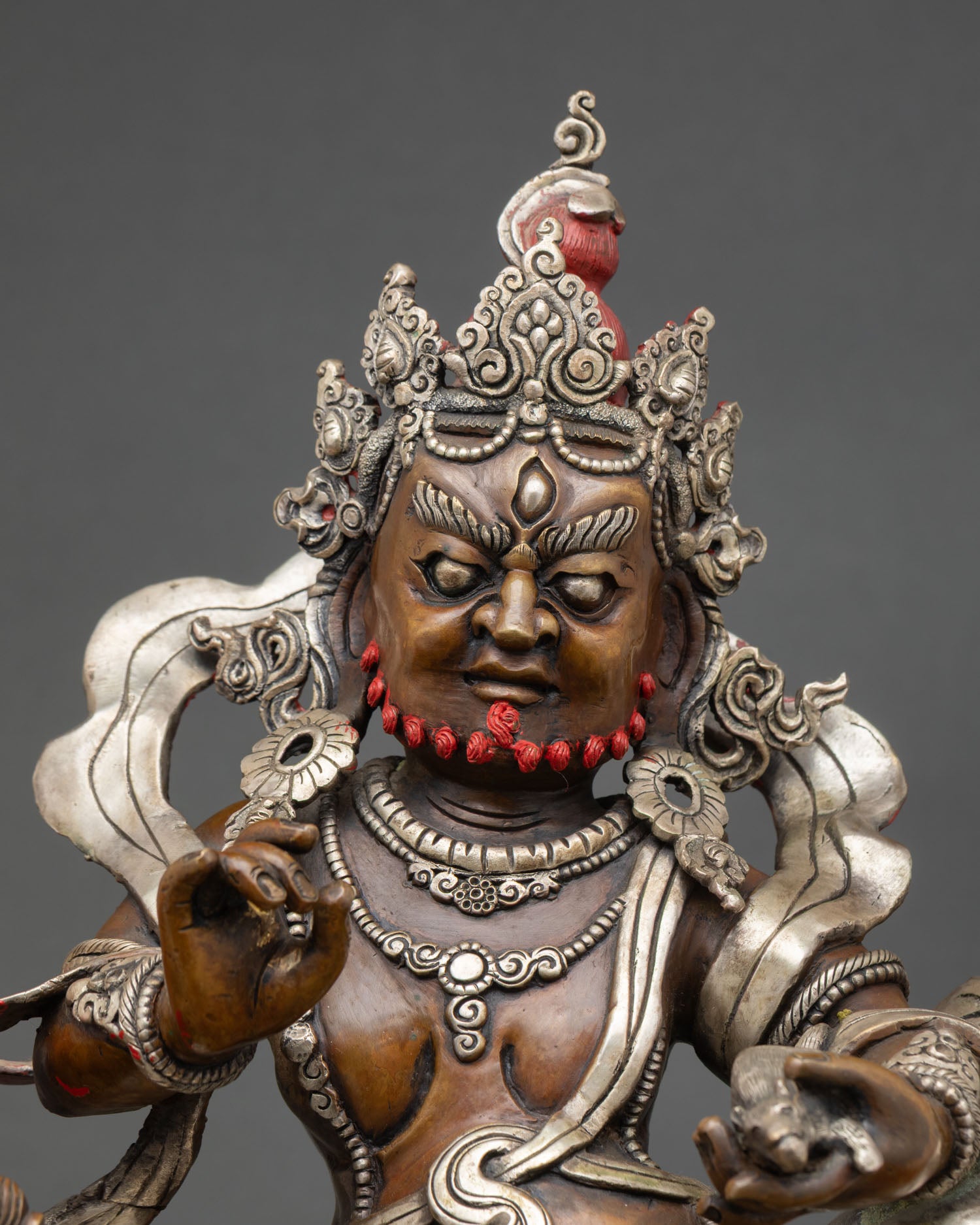 Close up of Namtoshe wealth deity statue with silver-plated ornaments and lotus throne details