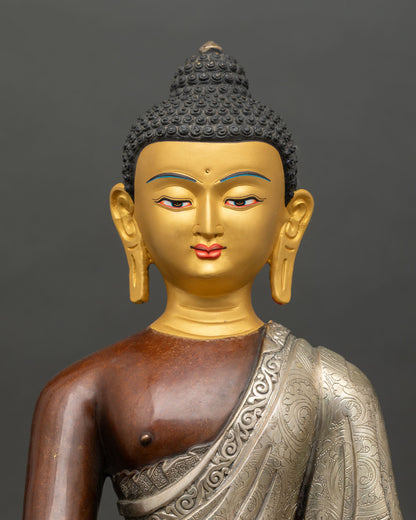 Close up of Nepalese Shakyamuni Buddha sculpture showing detailed silver-plated robe and serene gold-painted face