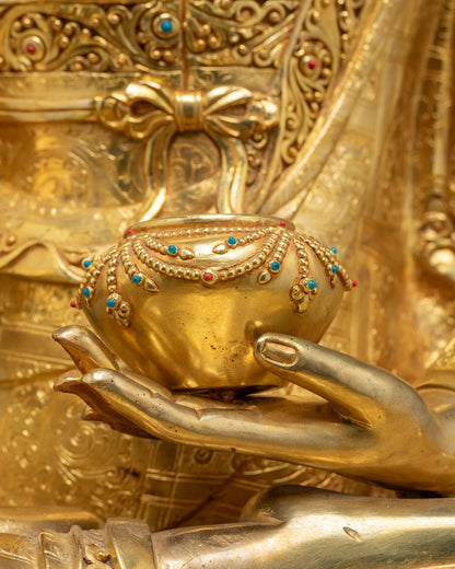 Close-up of turquoise and coral inlaid alms bowl held by gold Buddha statue