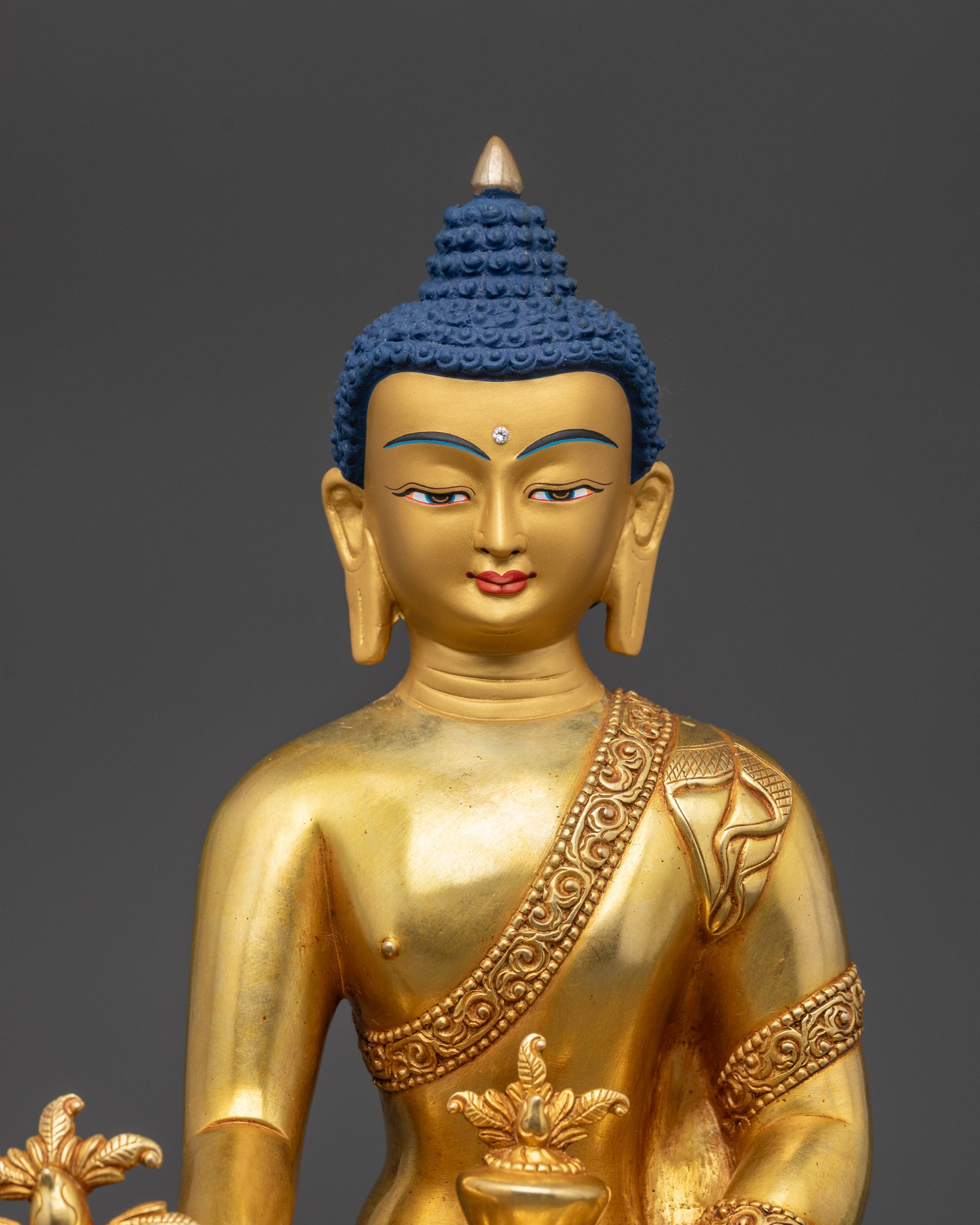 Close-up of 24K gold-gilded face and carved robe patterns of Medicine Buddha
