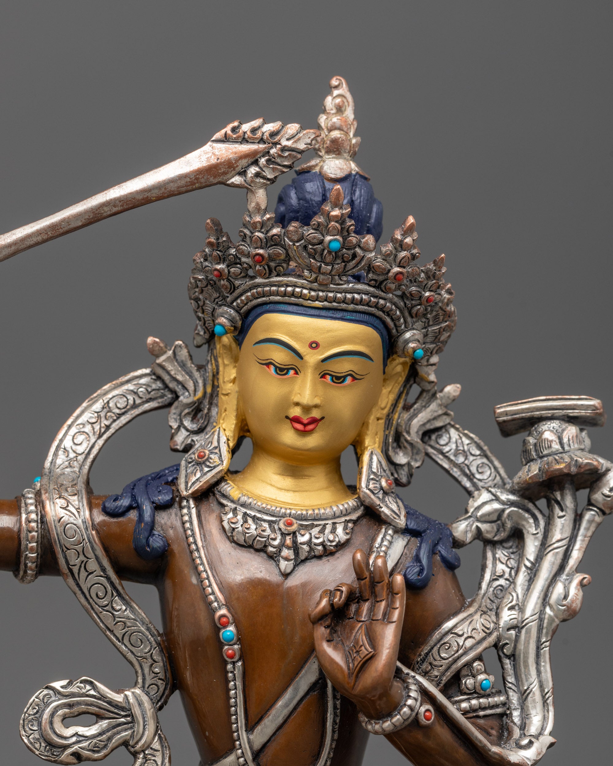 Close-up of 24K gold-gilded face on oxidized Manjushri statue with semi-precious stones