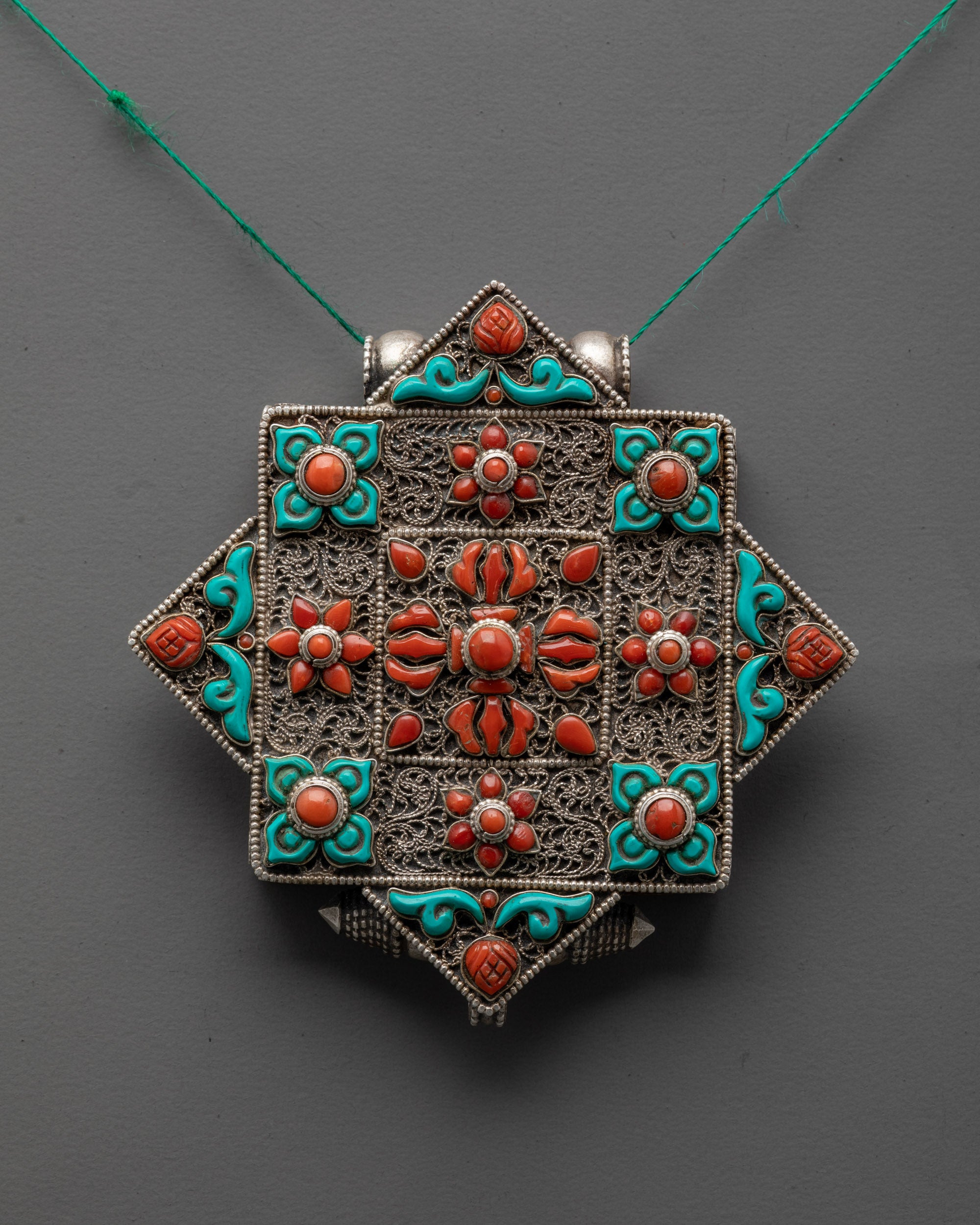 Close-up of Bishwo Vajra Locket showing intricate silver carving and coral double vajra centerpiece

