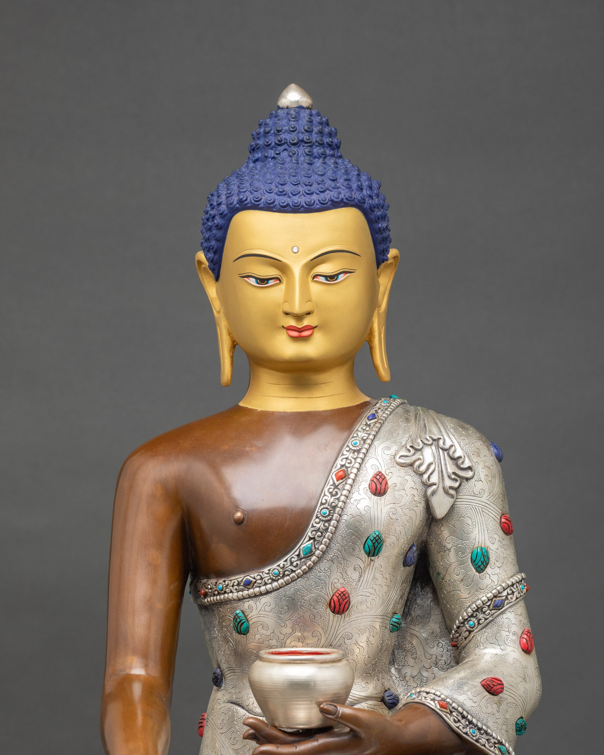 Close-up of Buddha holding monk’s bowl, adorned with semi-precious stones