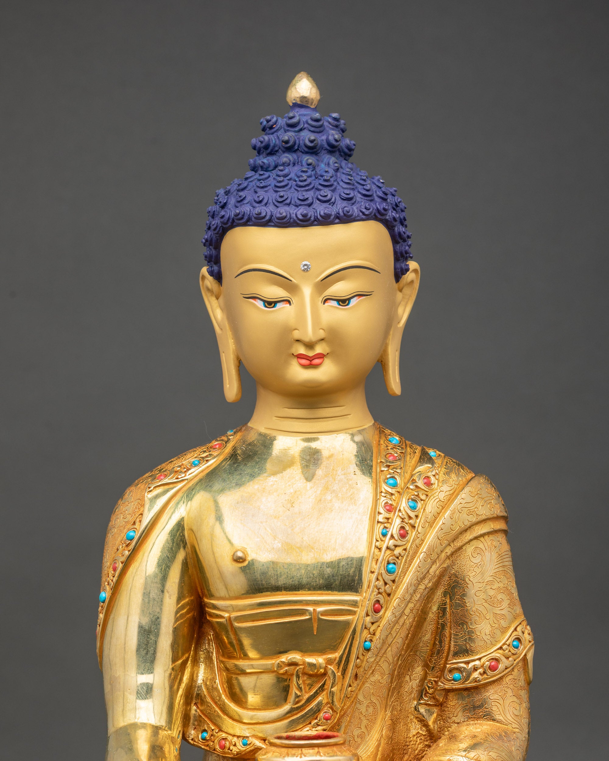 Close-up of Buddha statue face with 24k gold paint and semi-precious stone details, handcrafted in Patan, Nepal