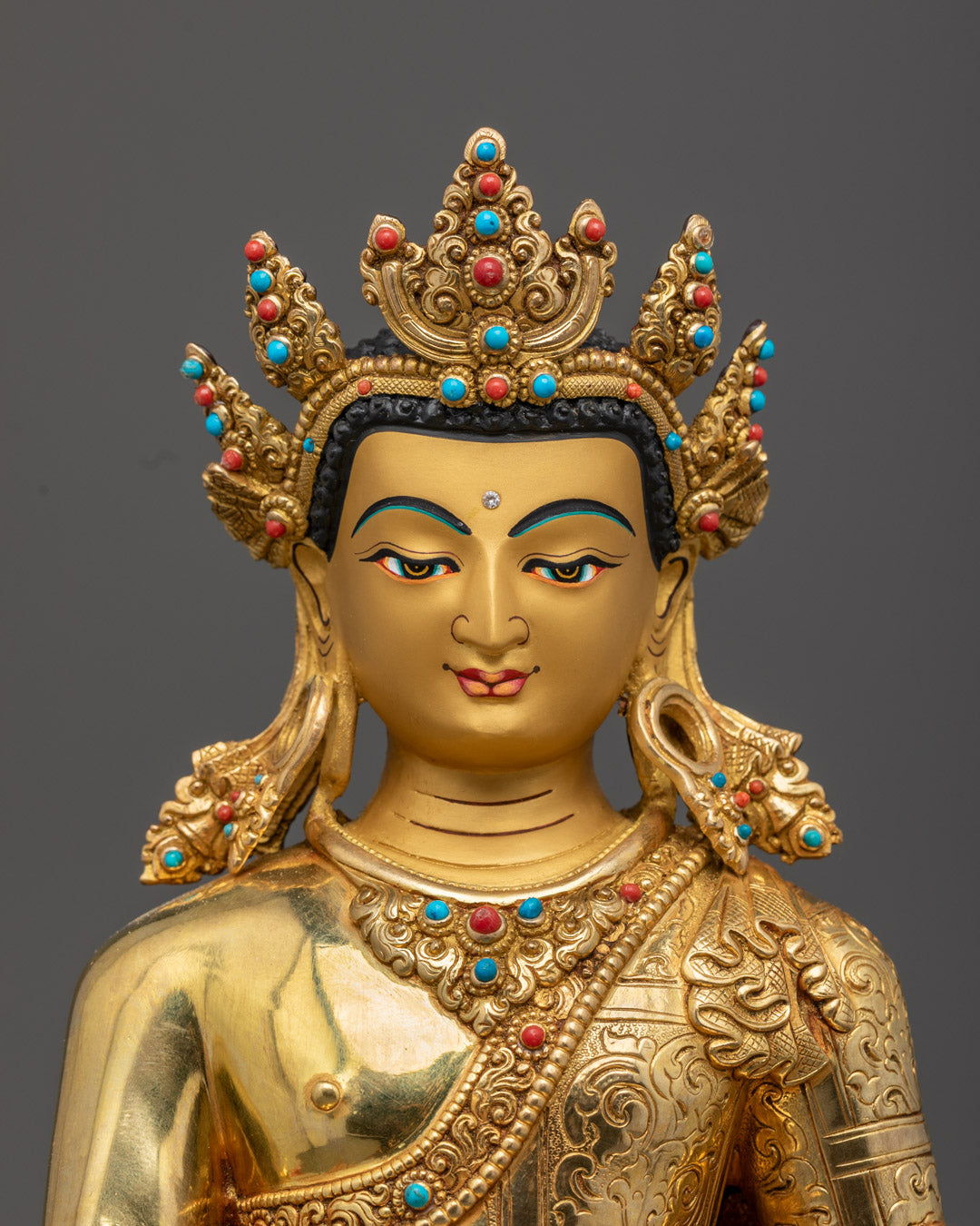 Close-up of Crowned Shakyamuni Buddha's serene face with 24K gold coating, adorned with semi-precious stones and rich acrylic colors, handmade in Nepal.