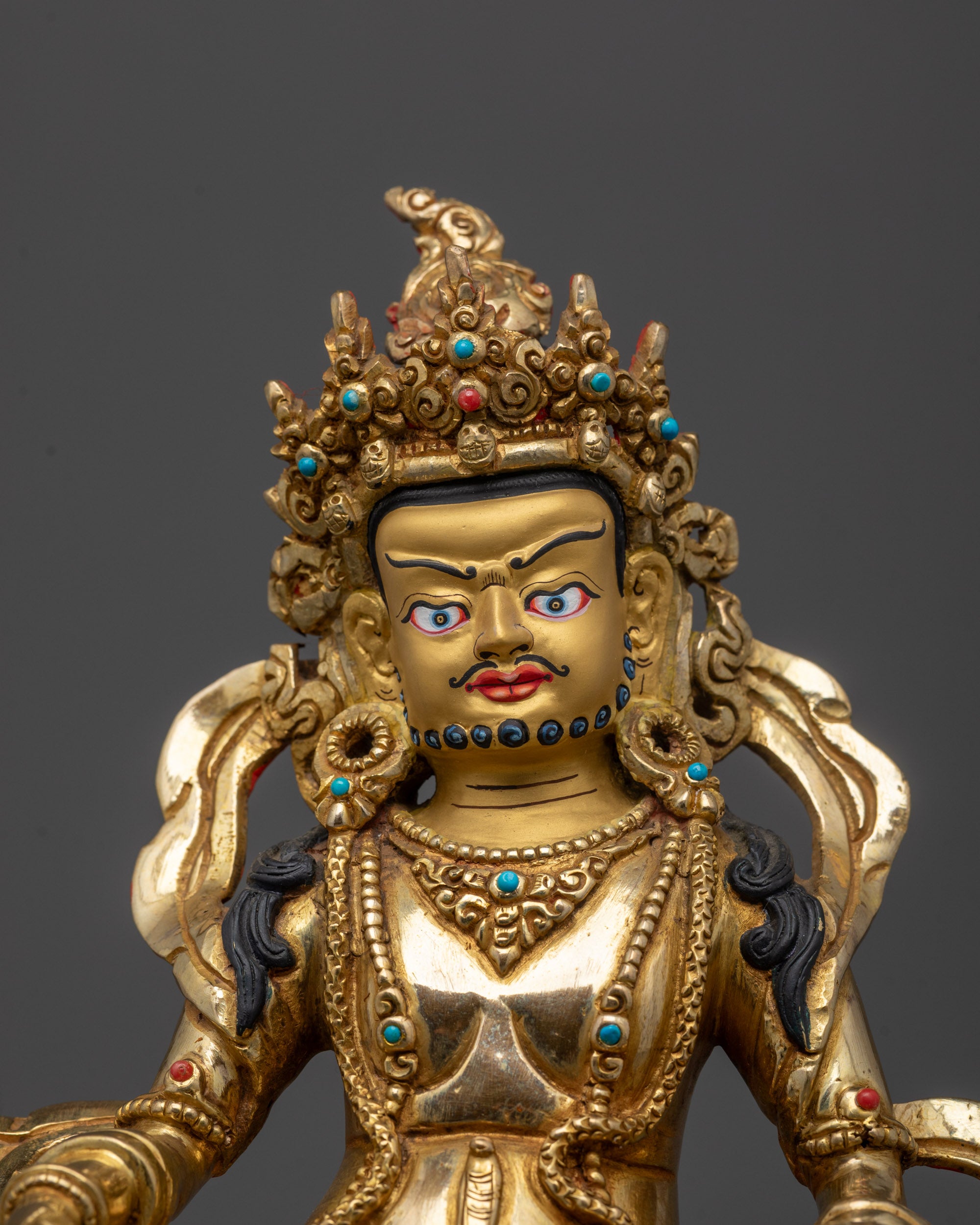 Close-up of Dzambhala's face showing intricate lost-wax detailing and vibrant gold finish