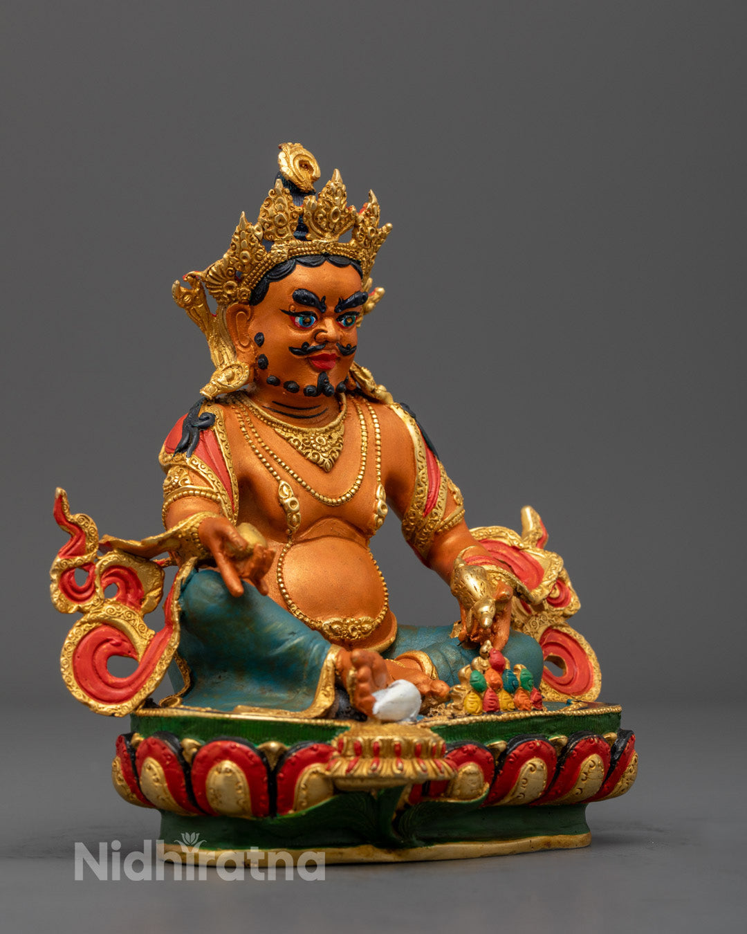 Dzambhala’s serene face adorned with semi-precious stones and golden highlights on copper statue.