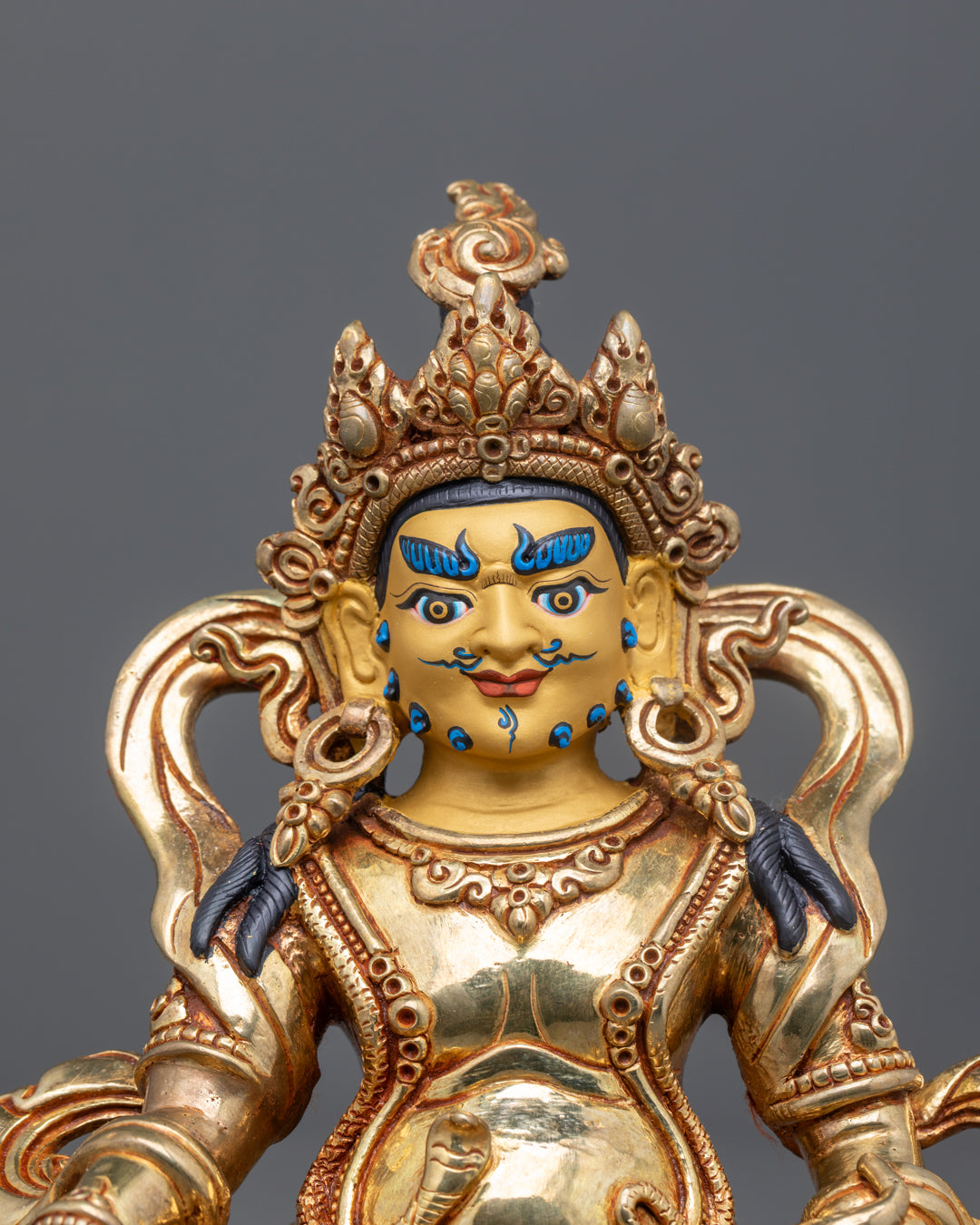 Dzambhala’s serene gold-gilded face with intricate hand-painted details and semi-precious stones