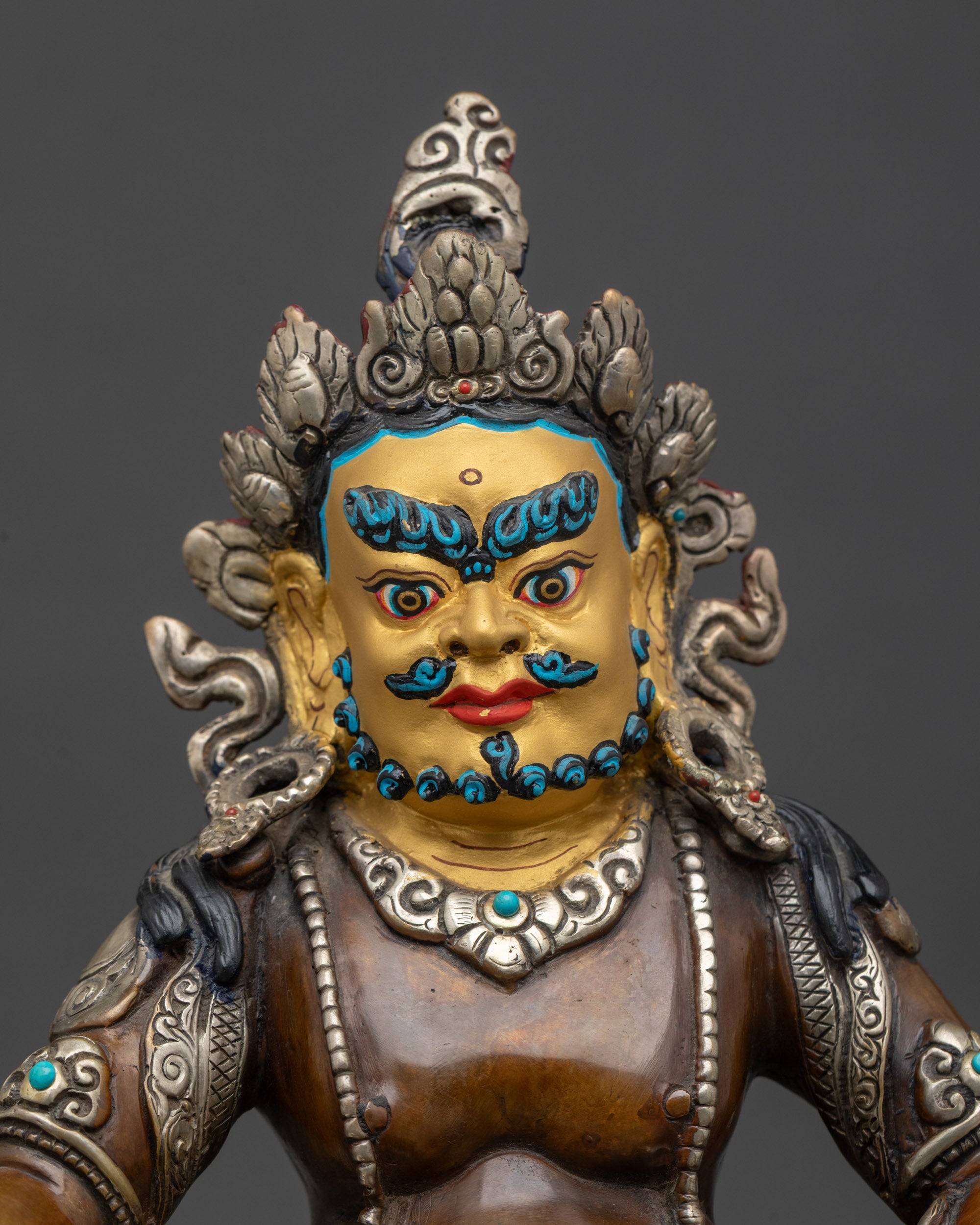Close-up of Dzambhala sculpture showing silver-plated finish and 24k gold face