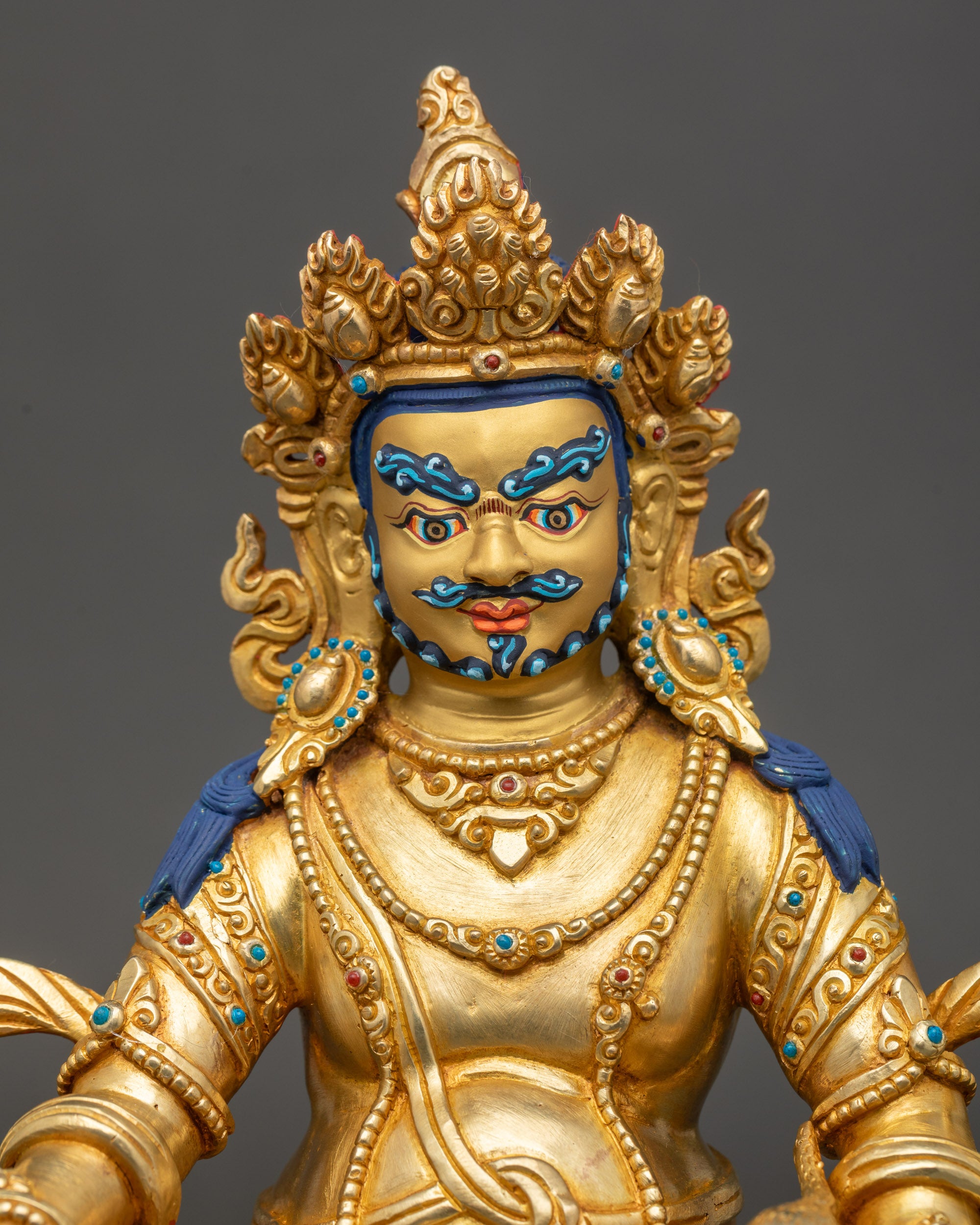 Close-up of Dzambhala statue face with gold paint and intricate gilded details