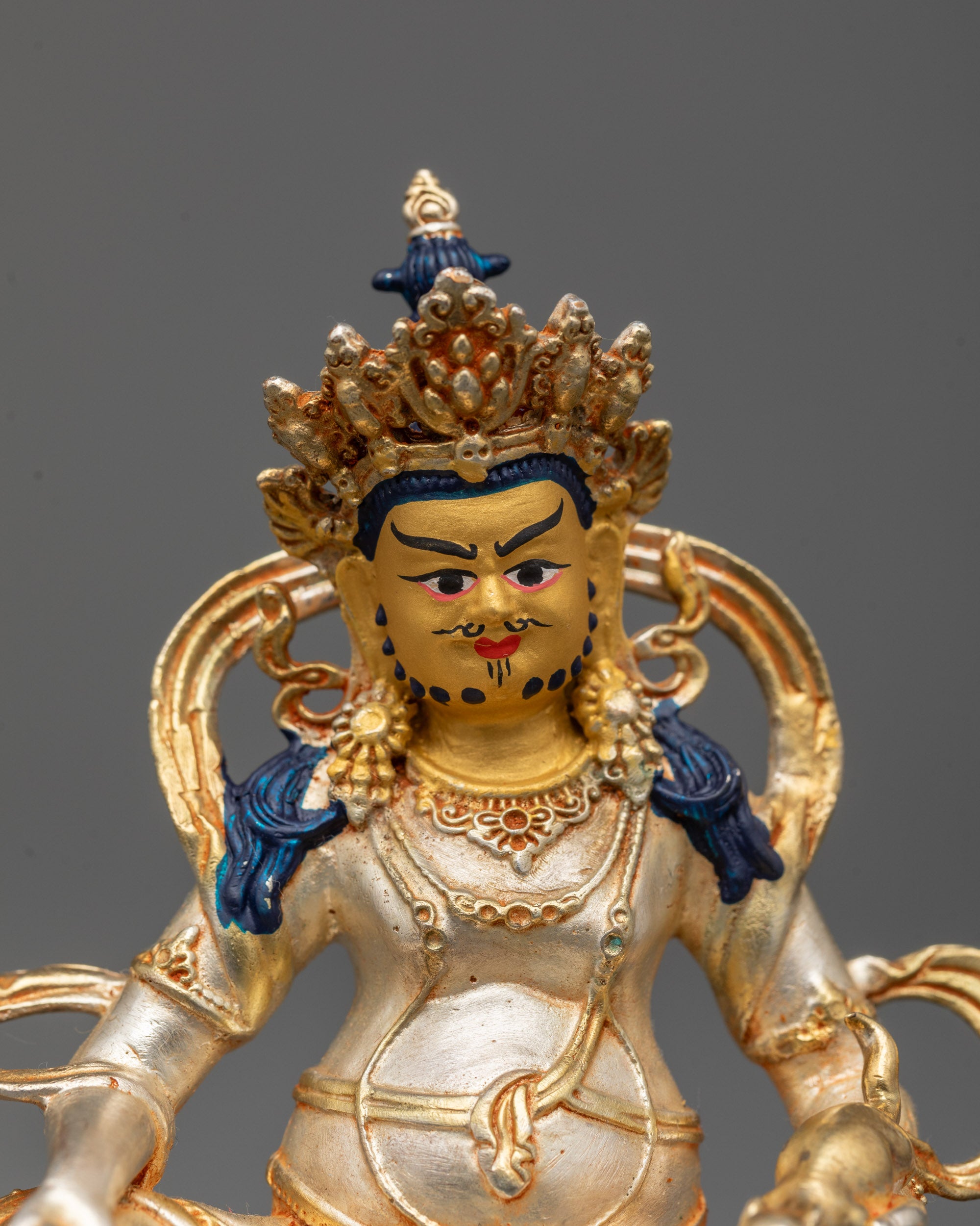 Close-up of Dzambhala statue’s five jeweled crown and flowing robe details
