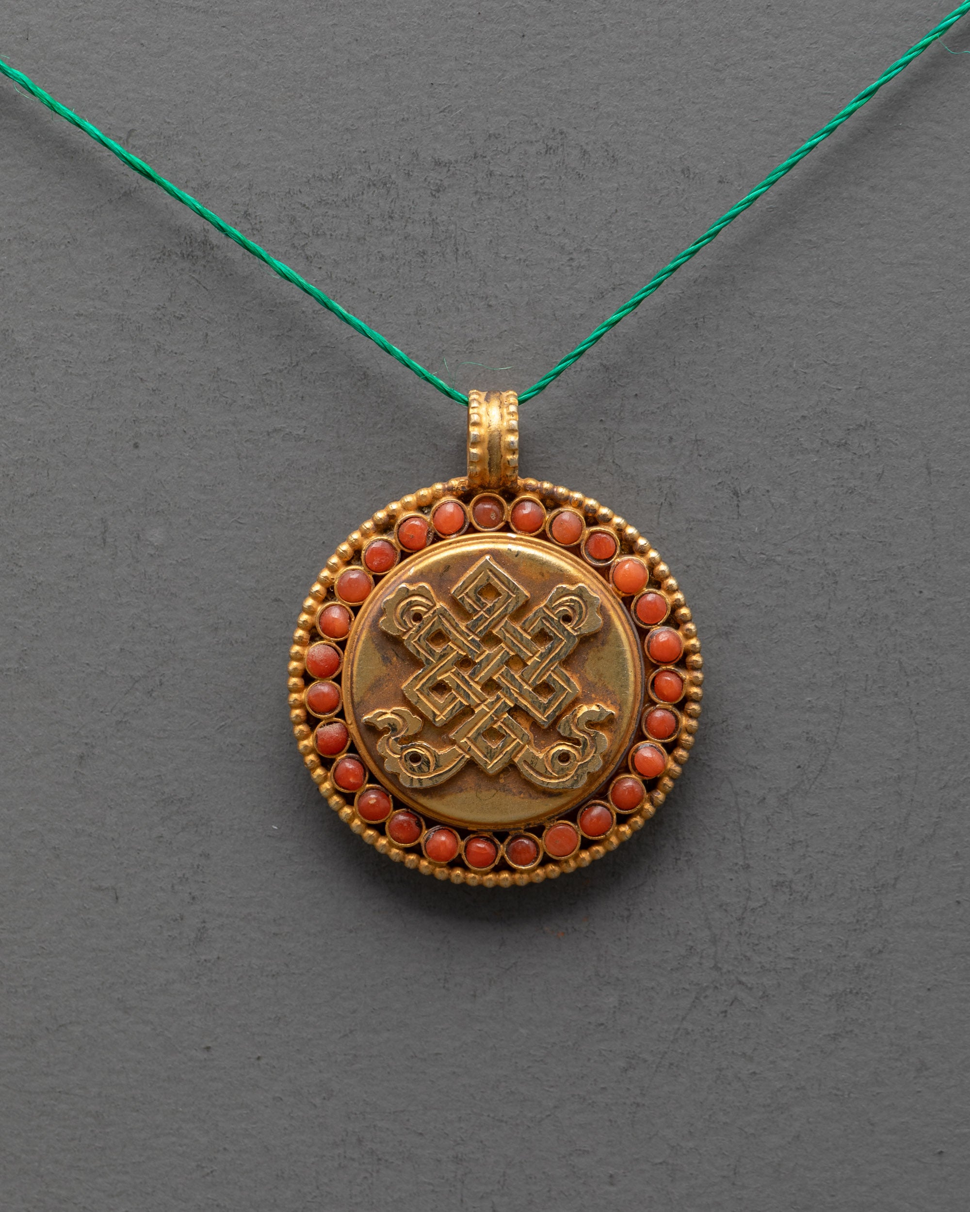 Close-up of Endless Knot Locket showing detailed carving and coral gemstone inlay