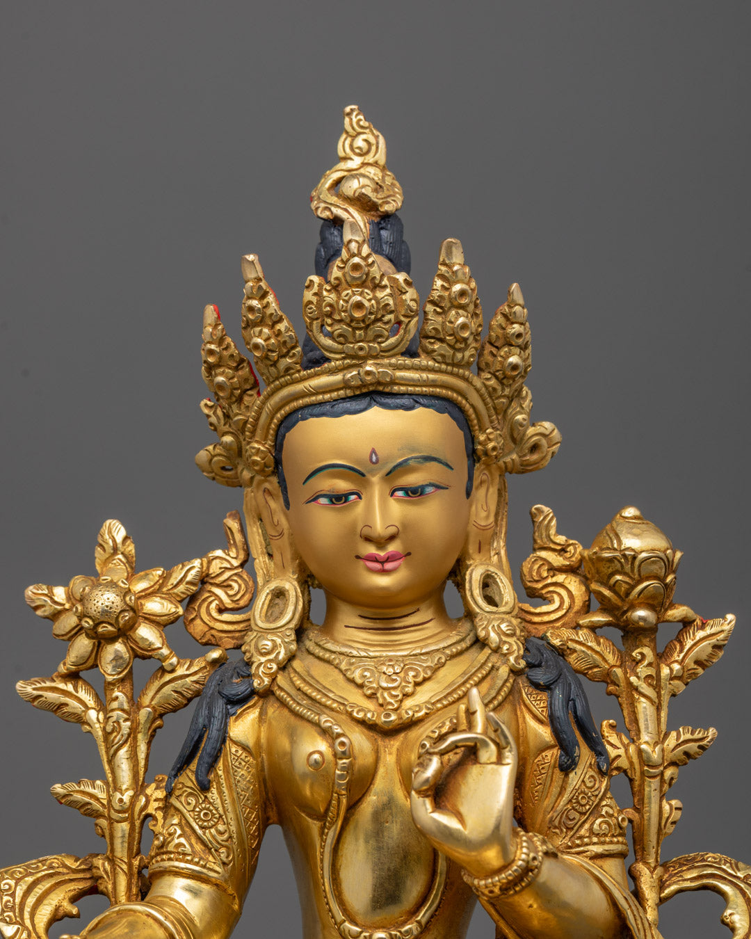 Close-up of Green Tara’s face and robe showing intricate carvings and fire-gilded details
