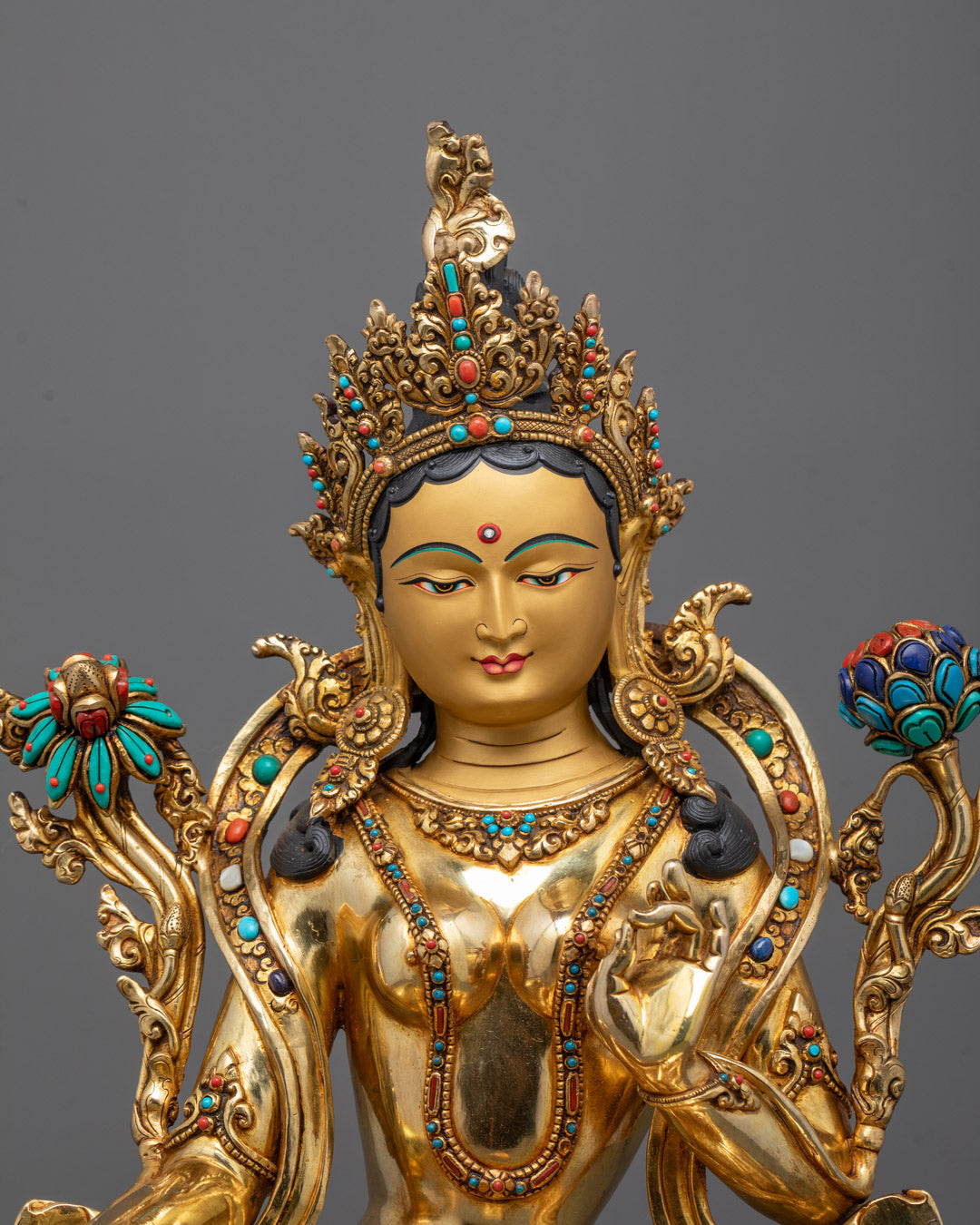 Close-up of Green Tara's serene gold-gilded face and intricate ornamentation