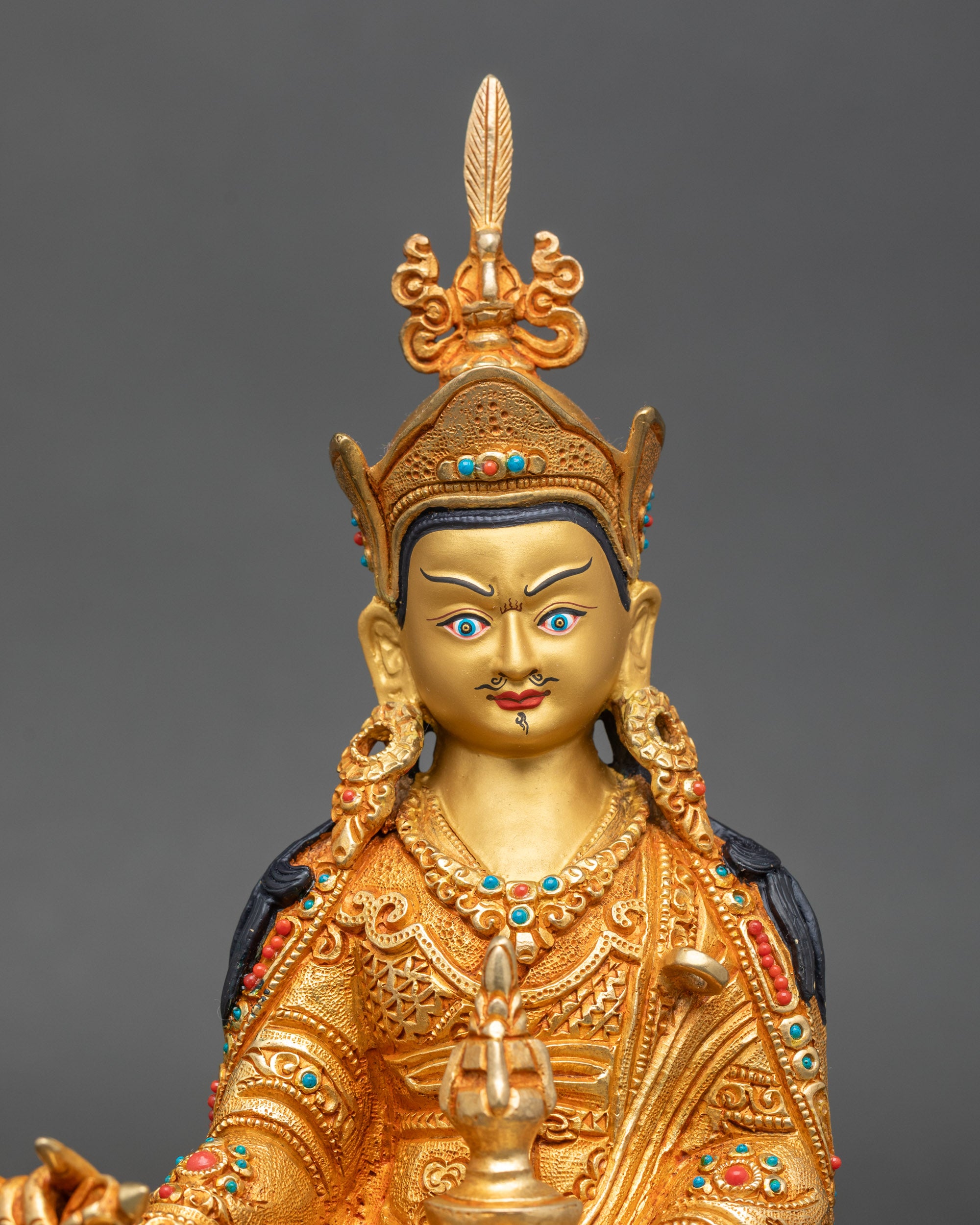 Close-up of Guru Rinpoche face showing serene expression and gold-painted detailing