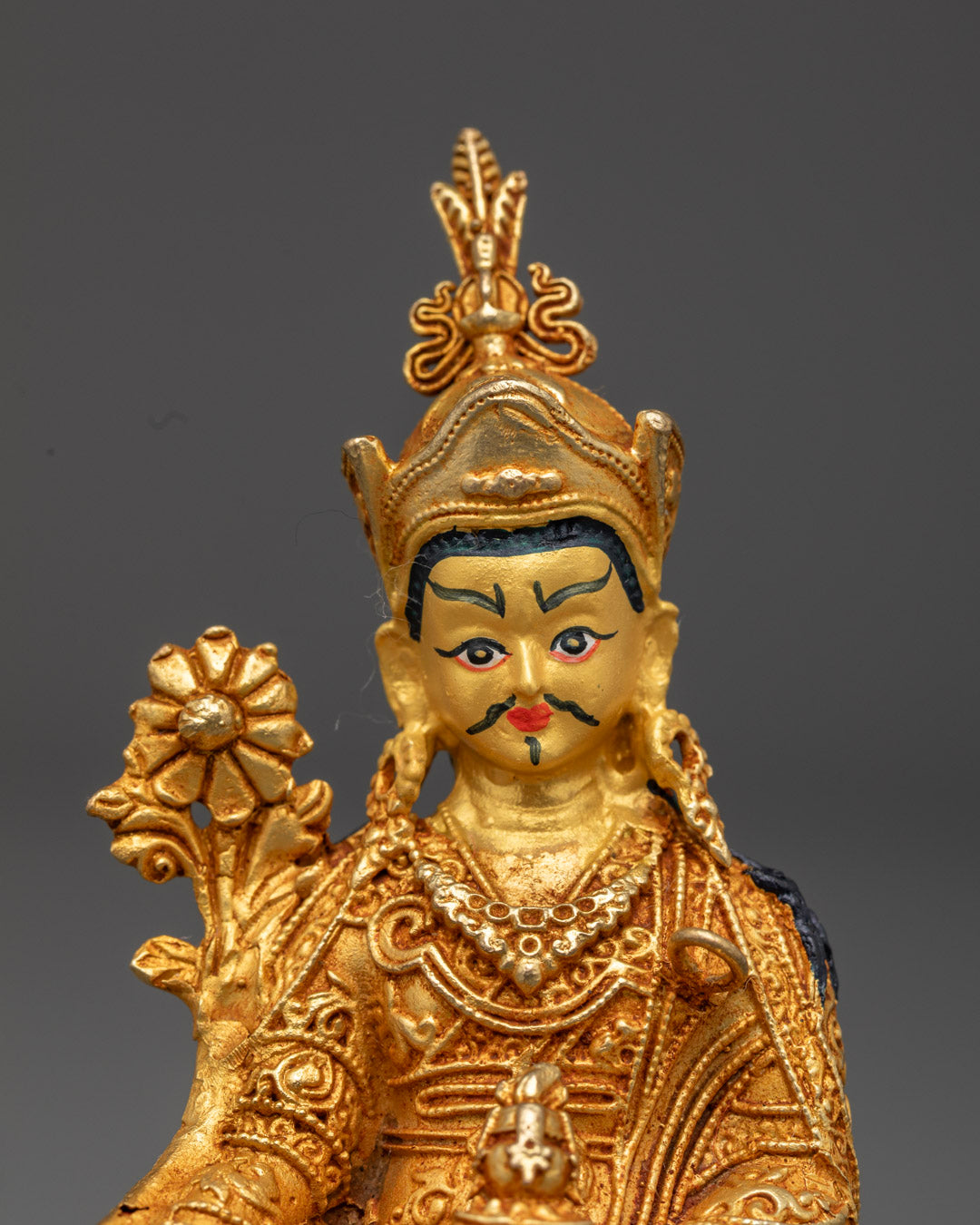 Close-up of Guru Rinpoche statue's gold face and acrylic-painted crown details
