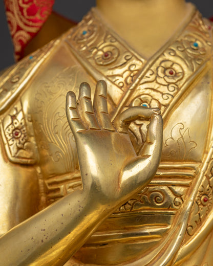 Close-up of Gyaltsab Je’s hand in Vitarka Mudra holding a scripture, with intricate robe and lotus throne details.