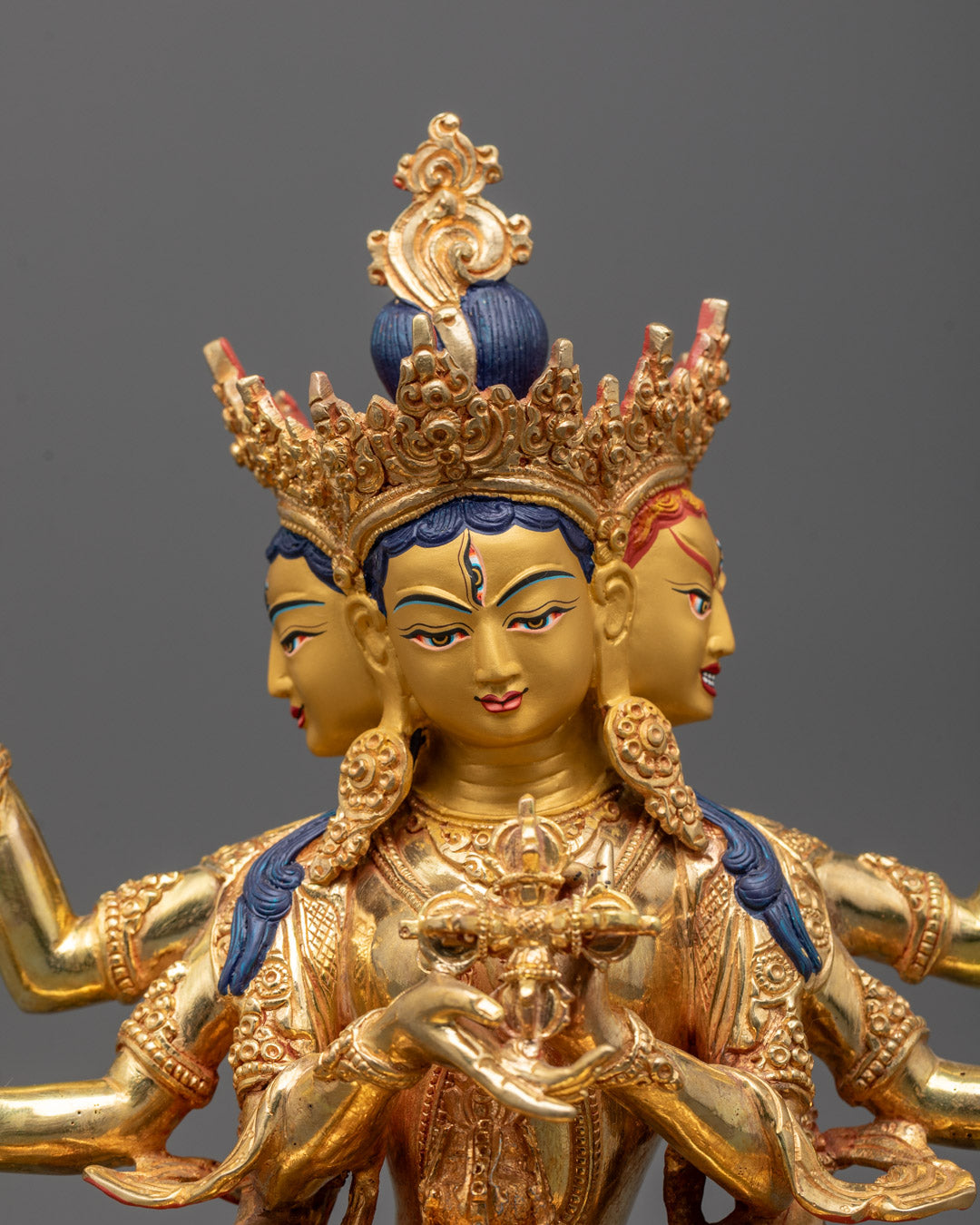 Close-up of Namgyalma’s serene gold-gilded face and detailed ritual objects held in multiple hands