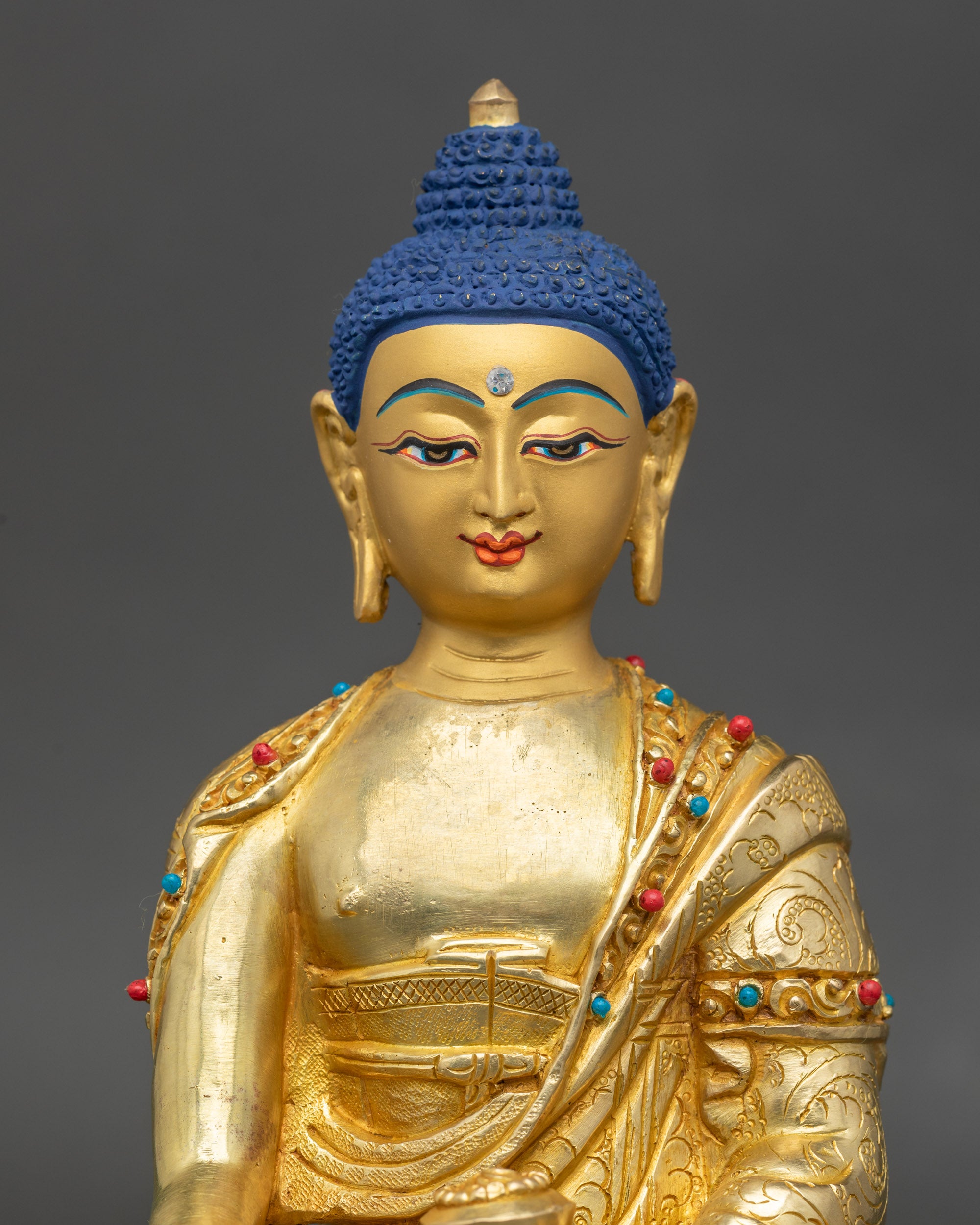 Close-up of Shakyamuni Buddha face showing serene expression, gold-painted details, and stones