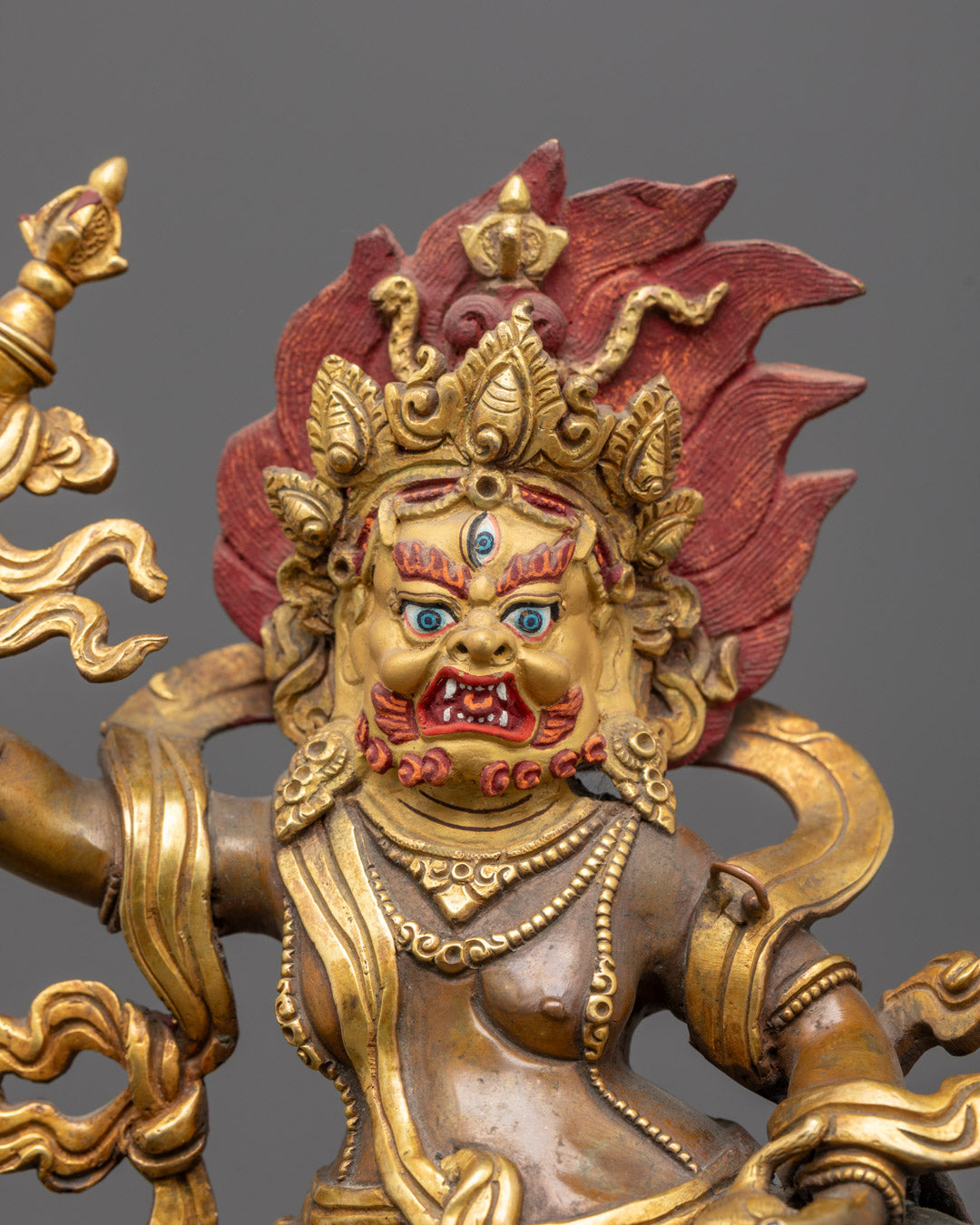 Close-up of White Dzambhala’s wrathful gold-gilded face with intricate carvings