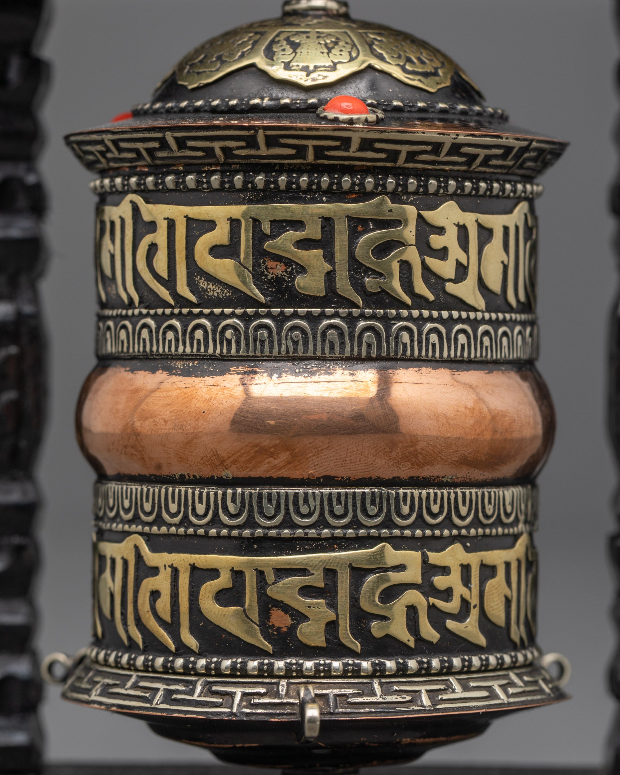 Close-up of engraved mantras and coral stones on copper Tibetan prayer wheel