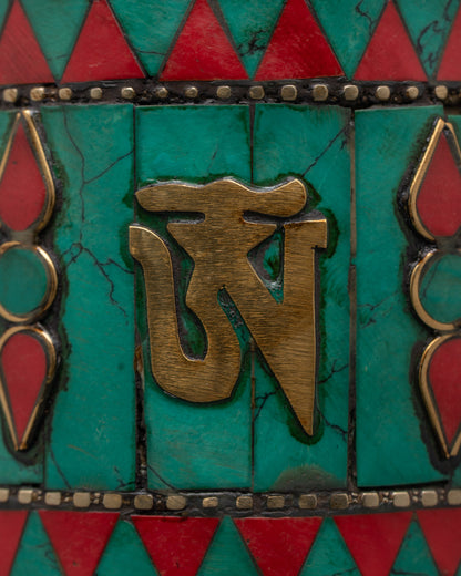 Close-up of engraved sacred mantras on copper prayer wheel with turquoise and coral inlays
