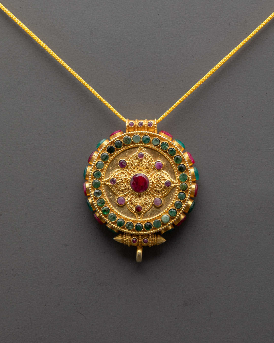 Close-up of gold-gilded Tibetan locket with intricate mandala design and coral stones